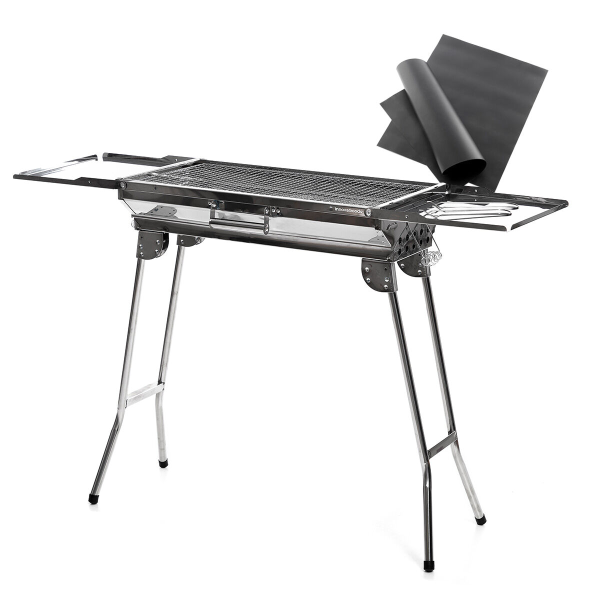 Silberner Metallgrill mit klappbaren Seitentabletts. Zwei schwarze Blätter liegen rechts.