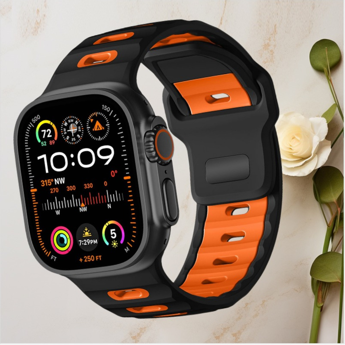 Smartwatch nero e arancione con display dettagliato, su sfondo chiaro con fiori.