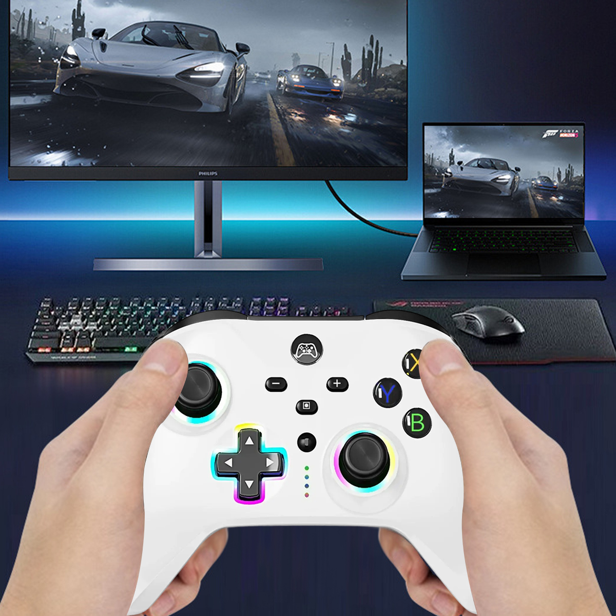 Hände halten einen weißen Gamecontroller. Ein Monitor und ein Laptop zeigen ein Rennspiel. Eine Tastatur und eine Maus sind sichtbar.