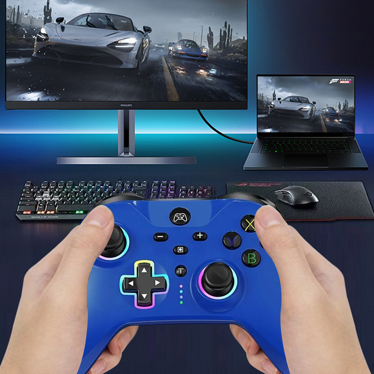 Hände halten einen blauen Controller, verbunden mit einem Monitor und Laptop.
