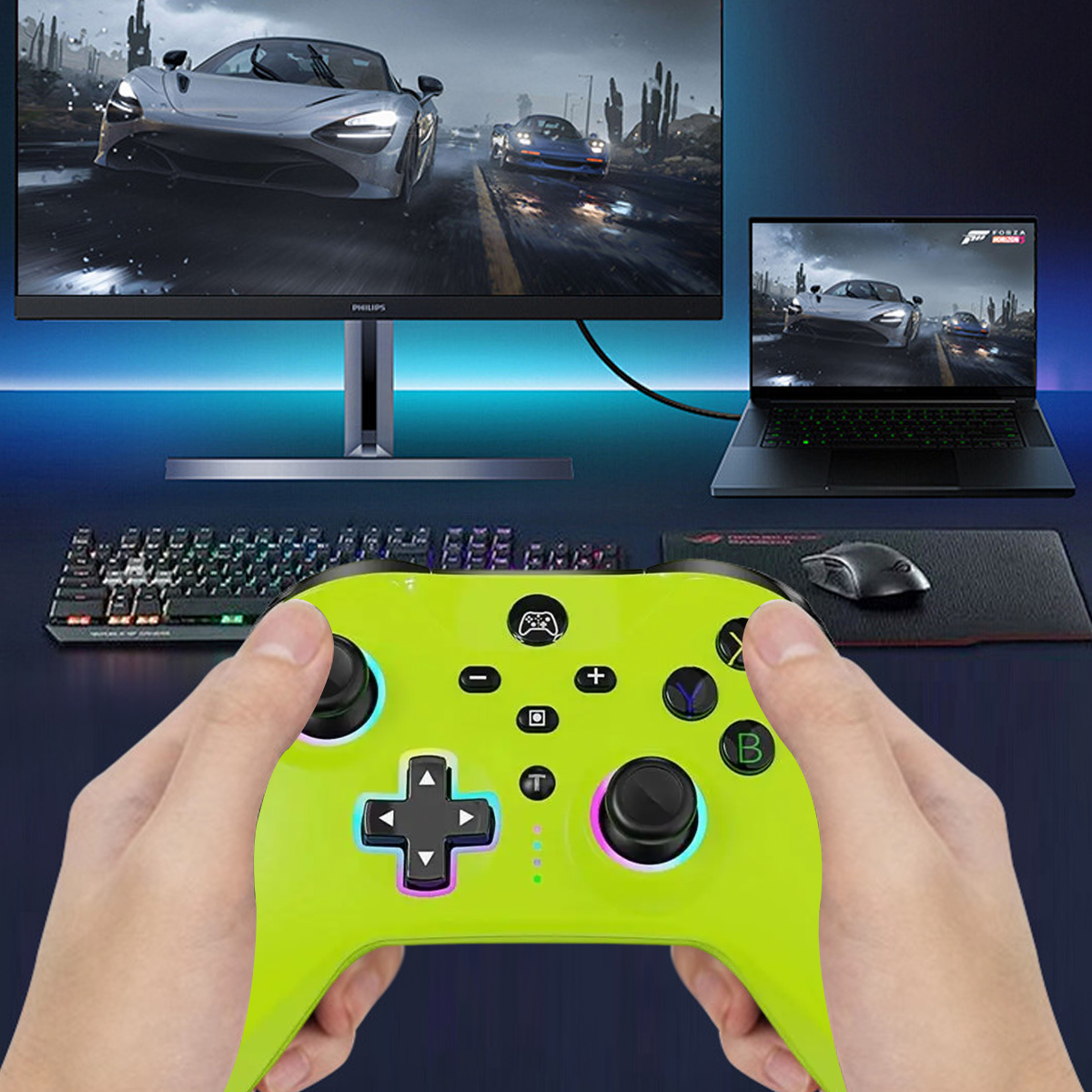 Eine Person hält einen grünen Gamecontroller. Im Hintergrund sind ein Monitor und ein Laptop zu sehen.