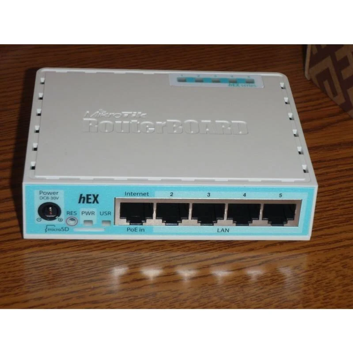 Enrutador RouterBOARD con múltiples puertos y texto. El enrutador es blanco y azul claro.