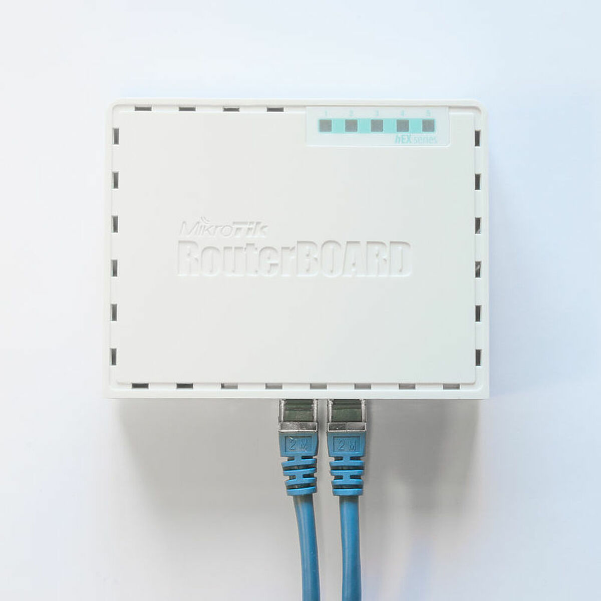 Un RouterBOARD MikroTik blanco con dos cables de red azules enchufados, sobre un fondo blanco.
