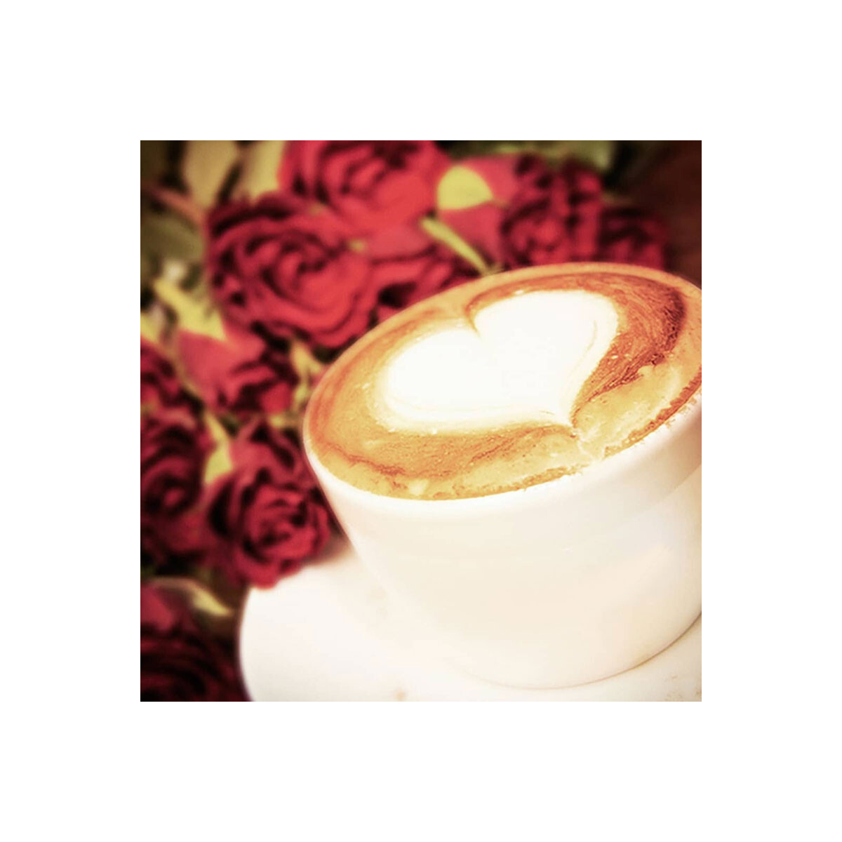 Eine weiße Tasse mit herzförmigem Design in Kaffee, vor rotem Rosenhintergrund.