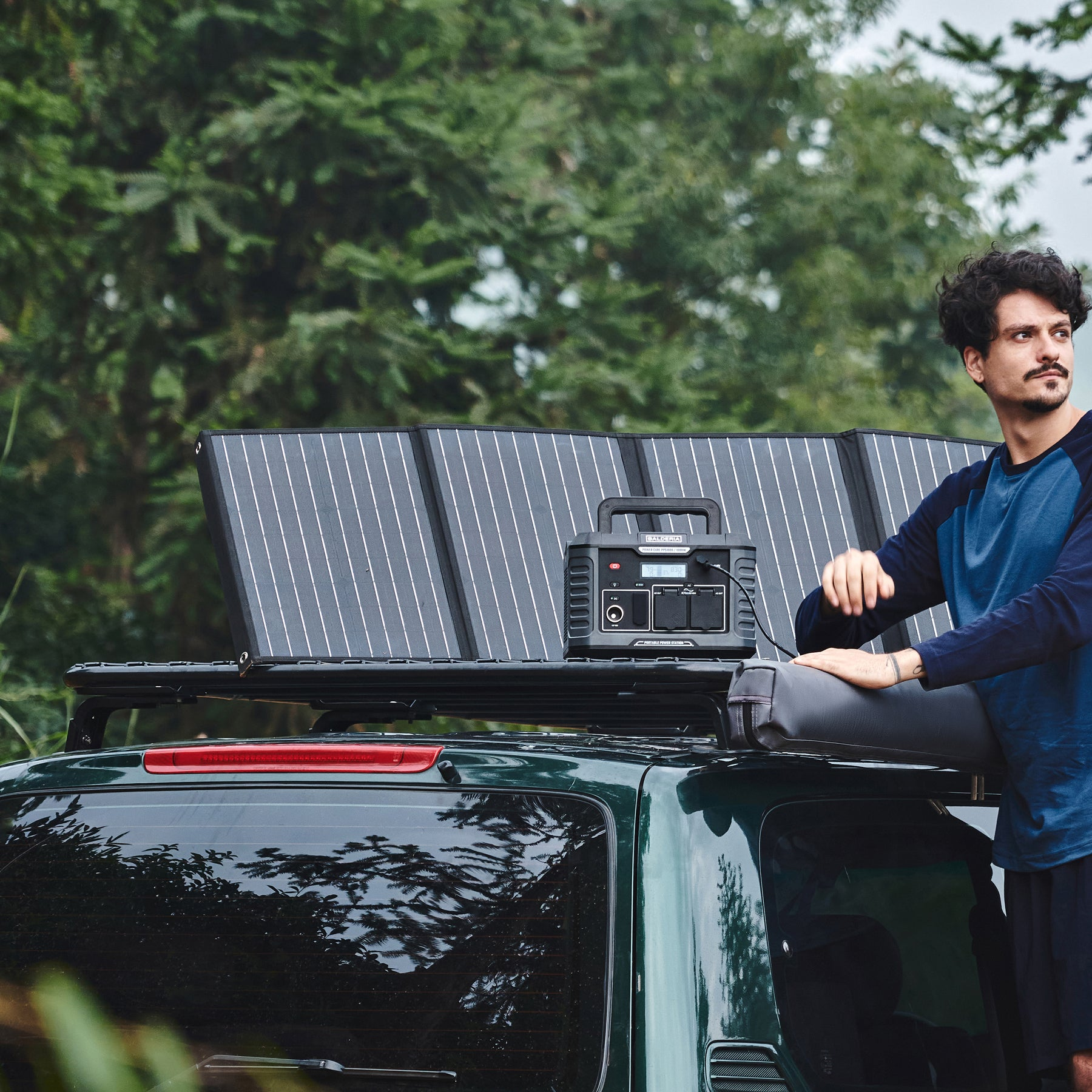 Ein Mann in der Nähe eines Autos mit Solarpanels. Er ist in der Nähe einer Powerstation, die mit den Panels verbunden ist.