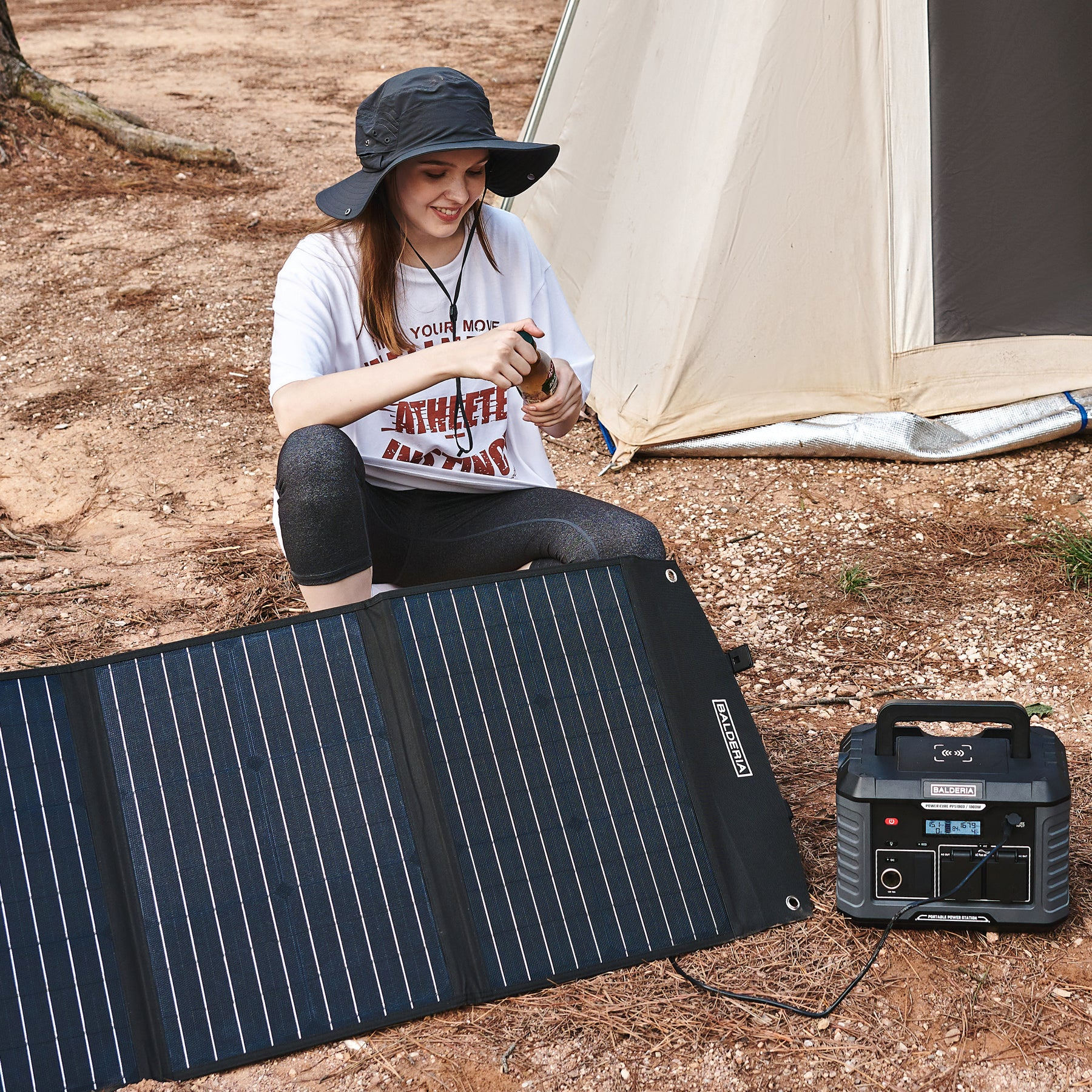 Frau mit Hut sitzt neben Zelt mit Solarpanel & Powerstation, umgeben von Kiefernnadeln.