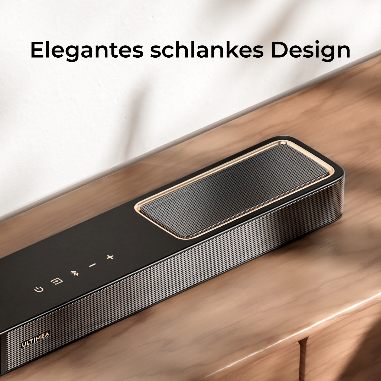 Czarny soundbar na drewnianej powierzchni. Srebrna siatkowa kratka i elementy sterujące na górze. Tekst: Elegancki smukły design.