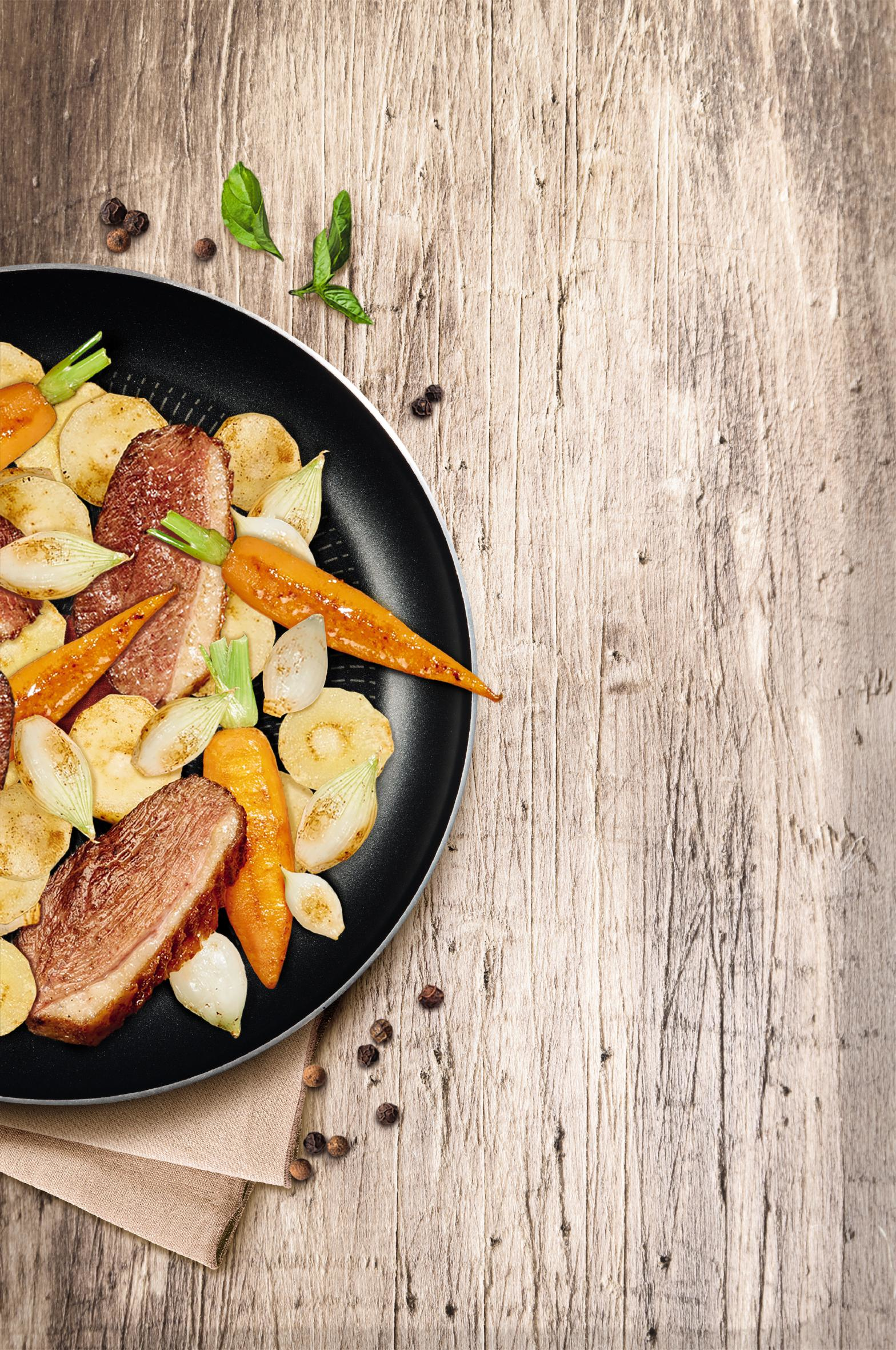 Pfanne mit gekochtem Essen: Karotten, Kartoffeln, Zwiebeln und Fleisch. Holz Hintergrund.