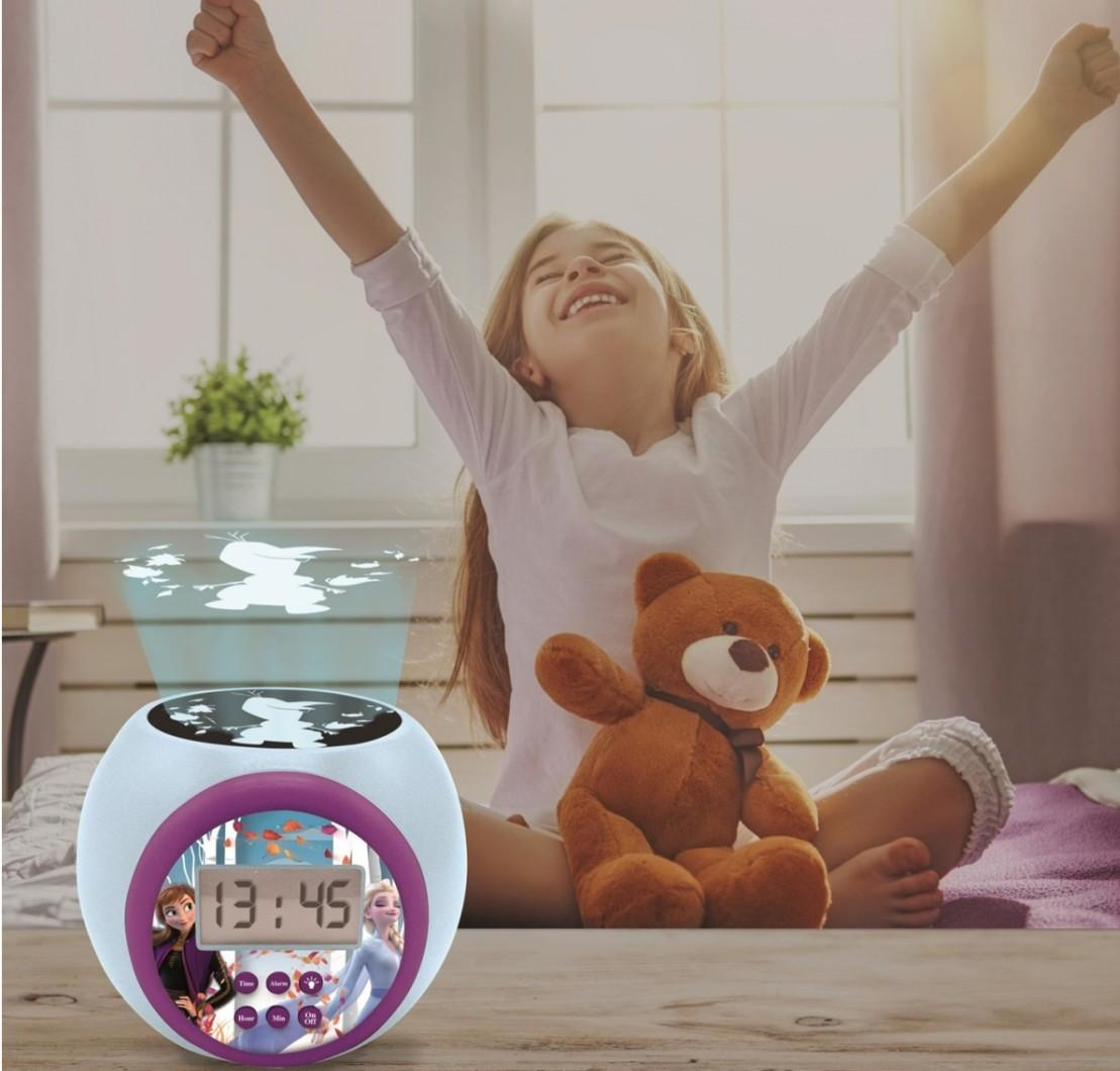 Ein Mädchen mit hochgestreckten Armen sitzt neben einem Wecker. Die Uhr zeigt die Zeit und hat Anna und Elsa.