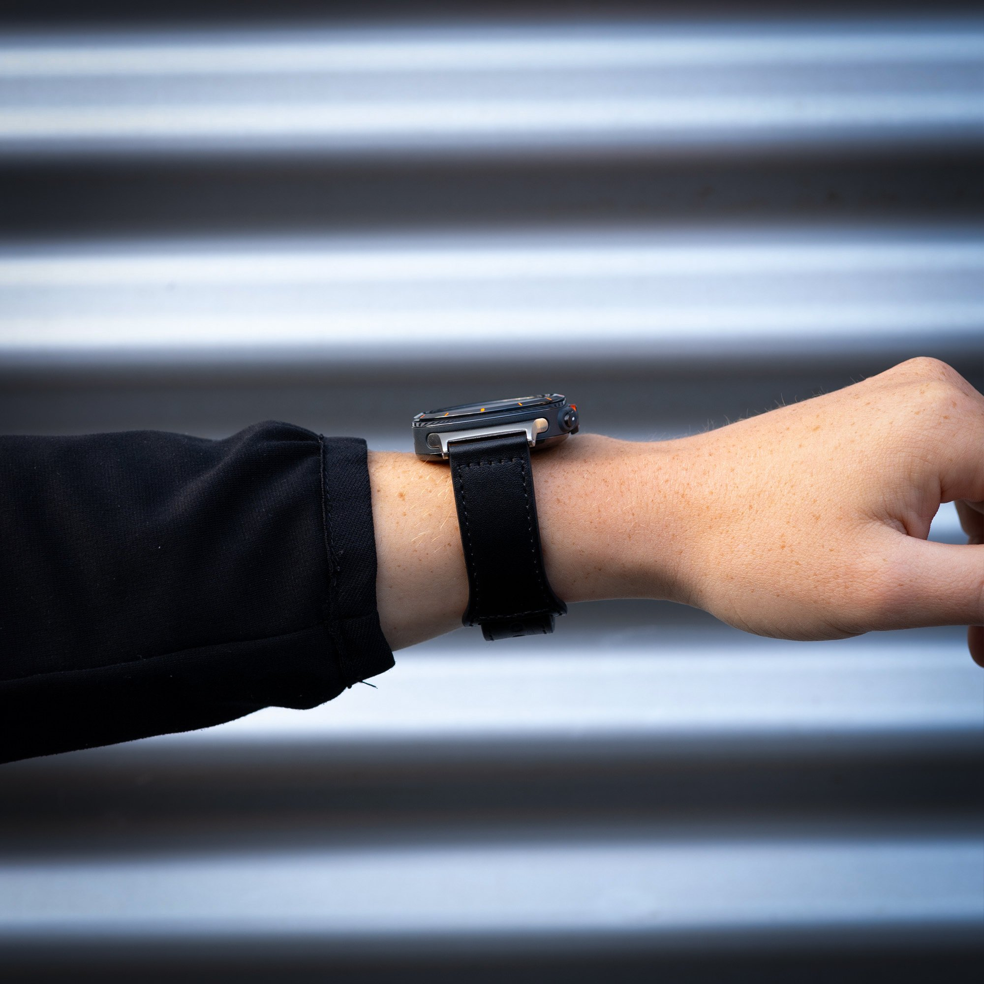Handgelenk mit schwarzer Uhr. Schwarzes Lederarmband. Grauer Hintergrund.