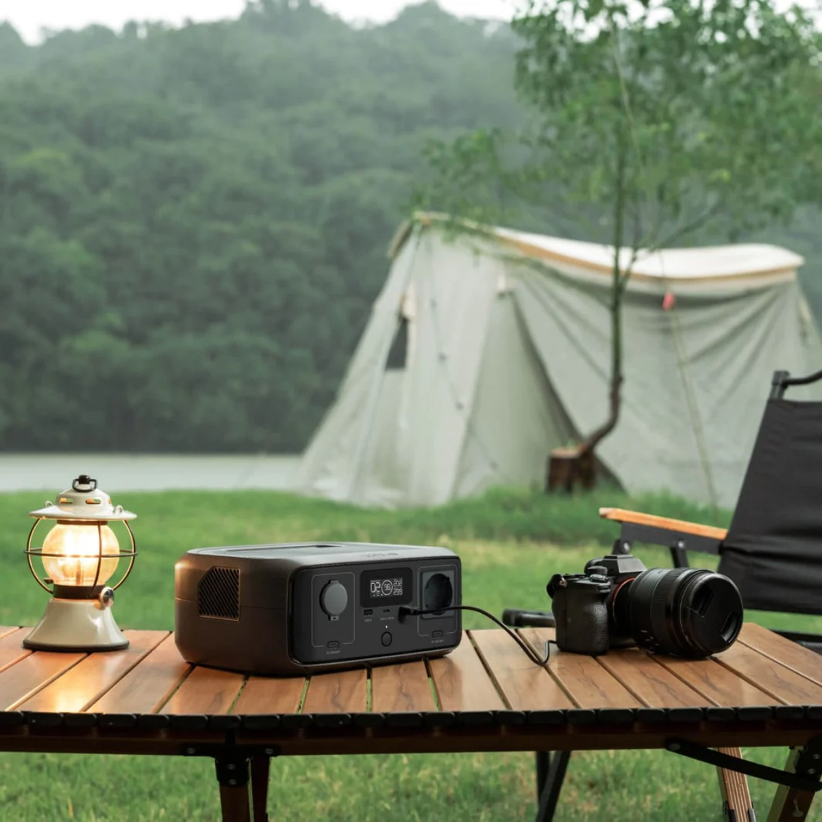 Scena kempingowa. Namiot, stół, latarnia, aparat i stacja zasilania znajdują się na stole.