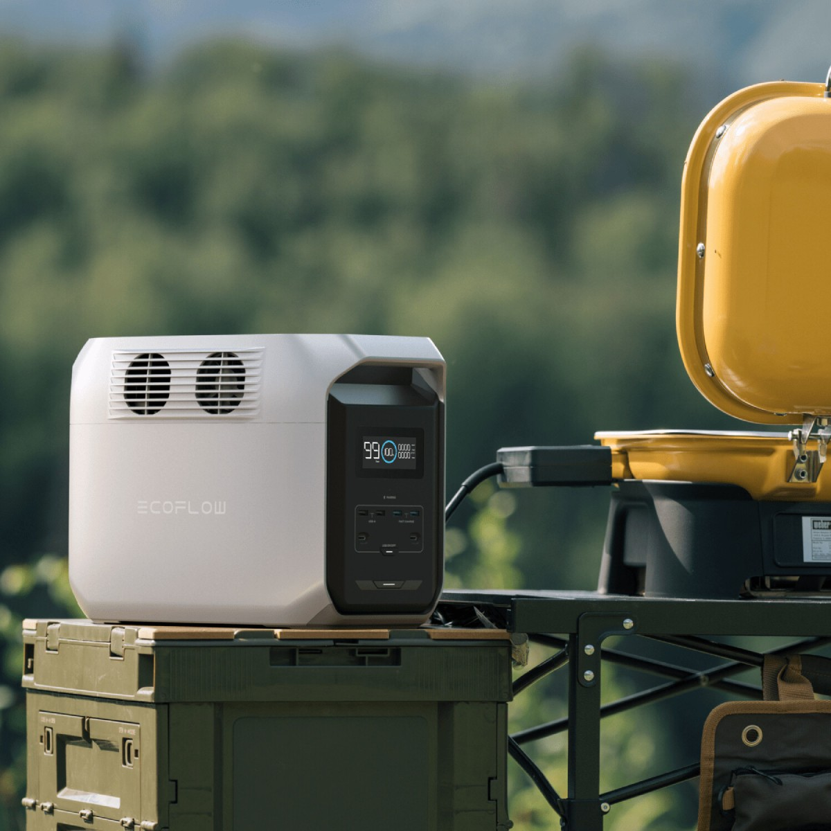 Przenośna stacja zasilania obok grilla i zielonego pojemnika. W otoczeniu zewnętrznym z drzewami.