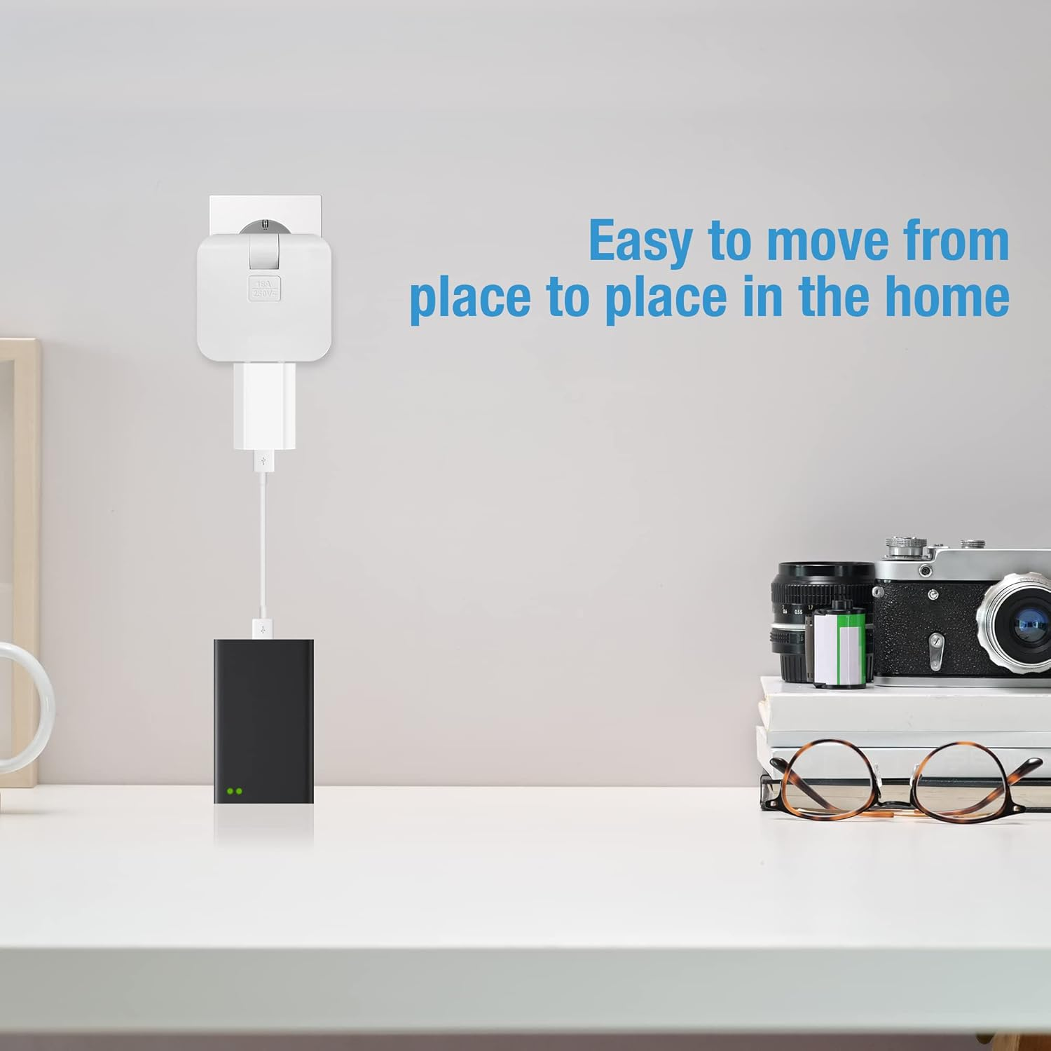Ein weißer Tisch mit einer schwarzen Powerbank, die an einen Stecker angeschlossen ist. Kamera und Brille.