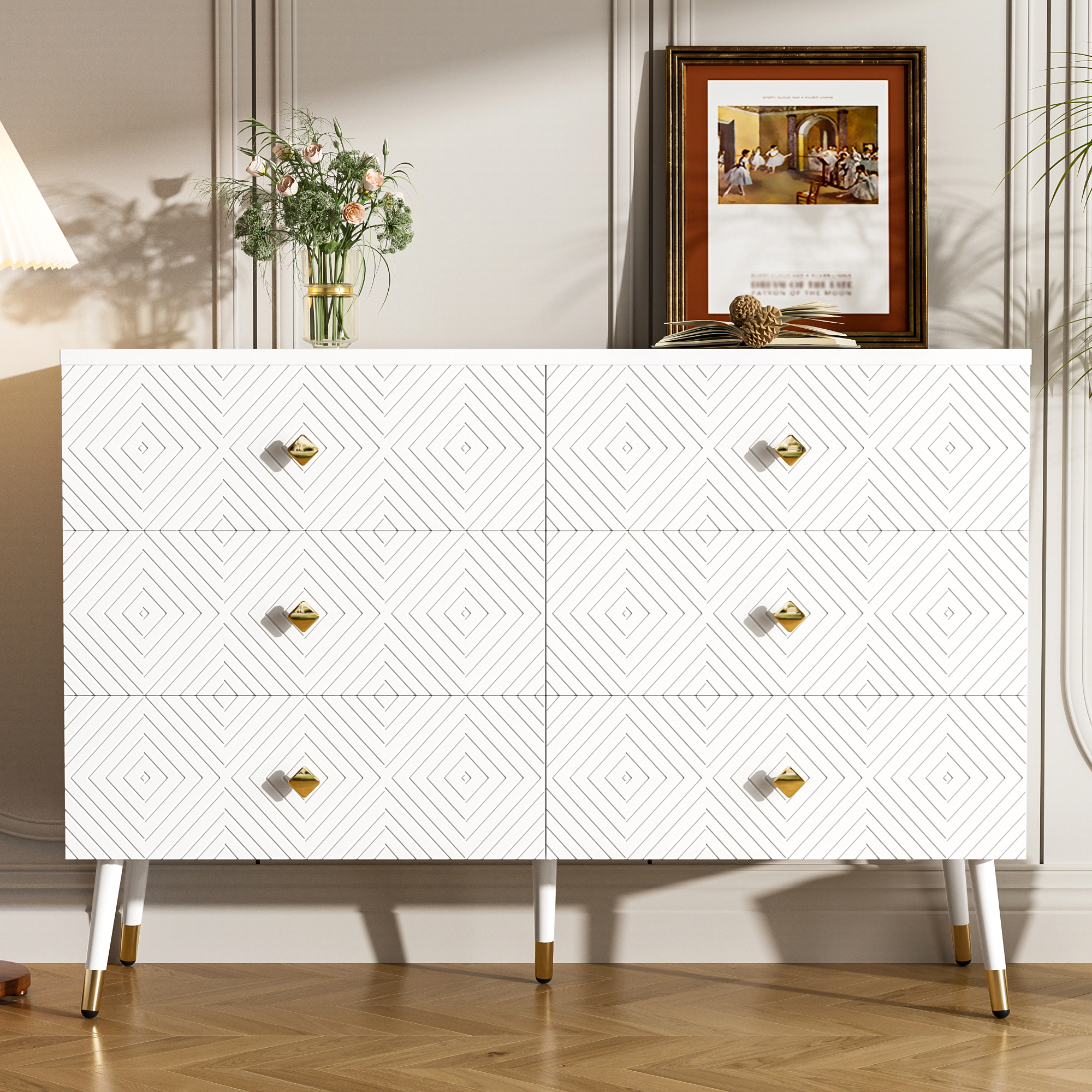 Weiße Kommode mit geometrischem Design, goldenen Knöpfen und Beinen. Es gibt eine Blumenvase und ein gerahmtes Bild.
