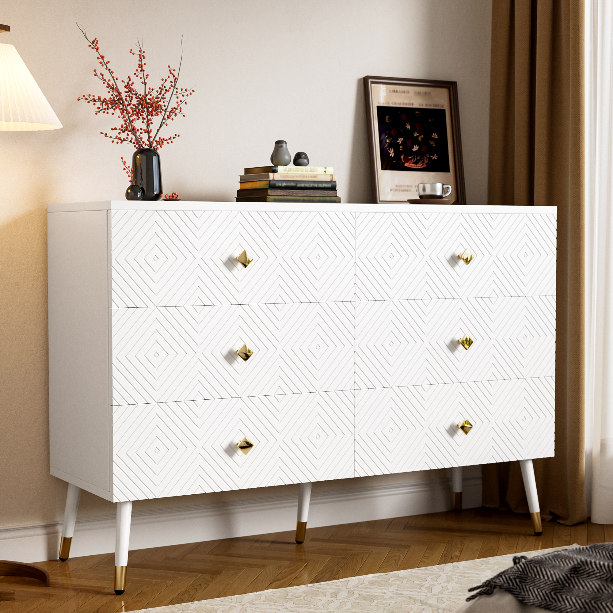 Weiße Kommode mit geometrischem Design, goldenen Knöpfen und Beinen. Schubladen sind geöffnet. Eine Lampe und Deko sind oben drauf.