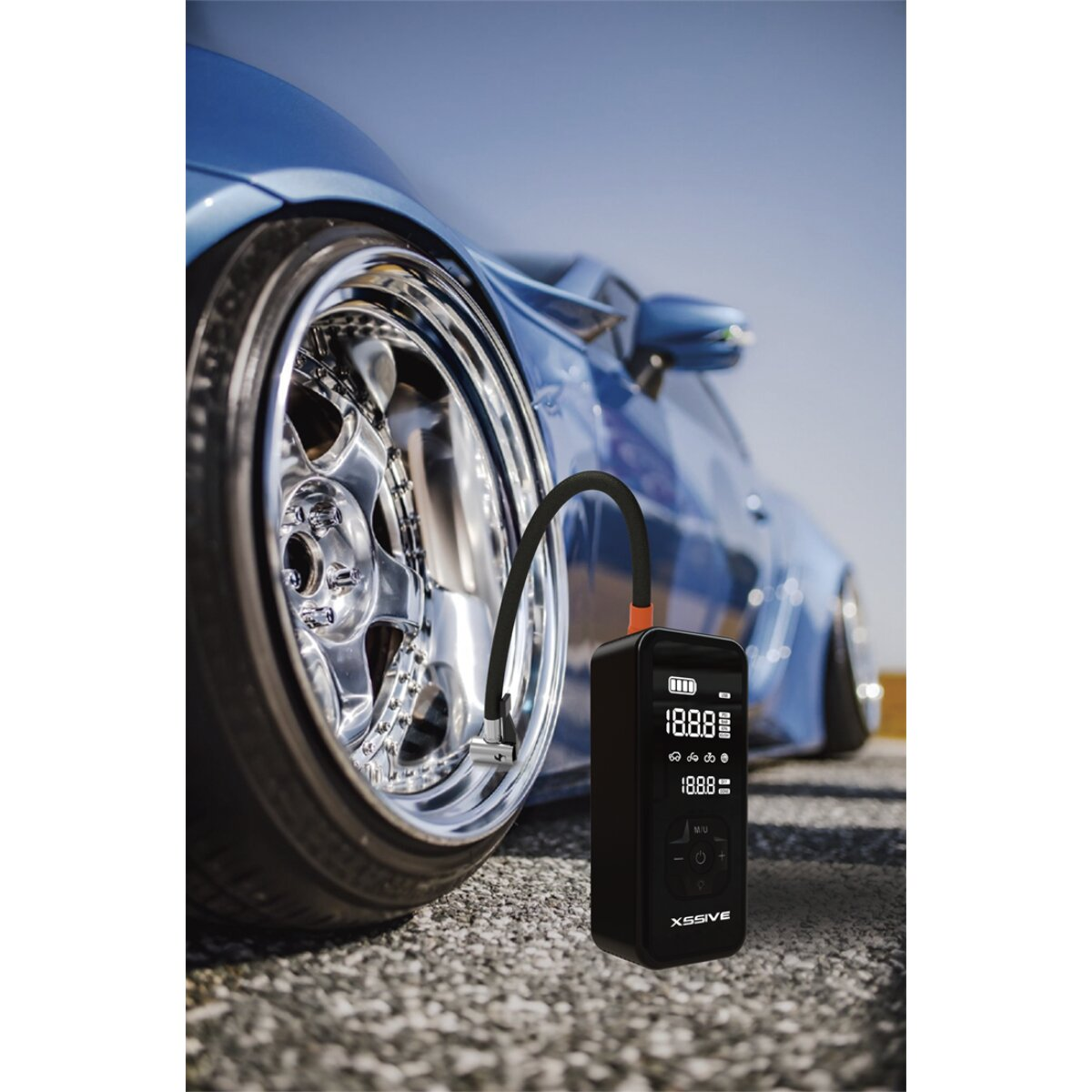 Eine schwarze tragbare Luftpumpe pumpt einen Autoreifen auf, mit einem blauen Auto im Hintergrund.