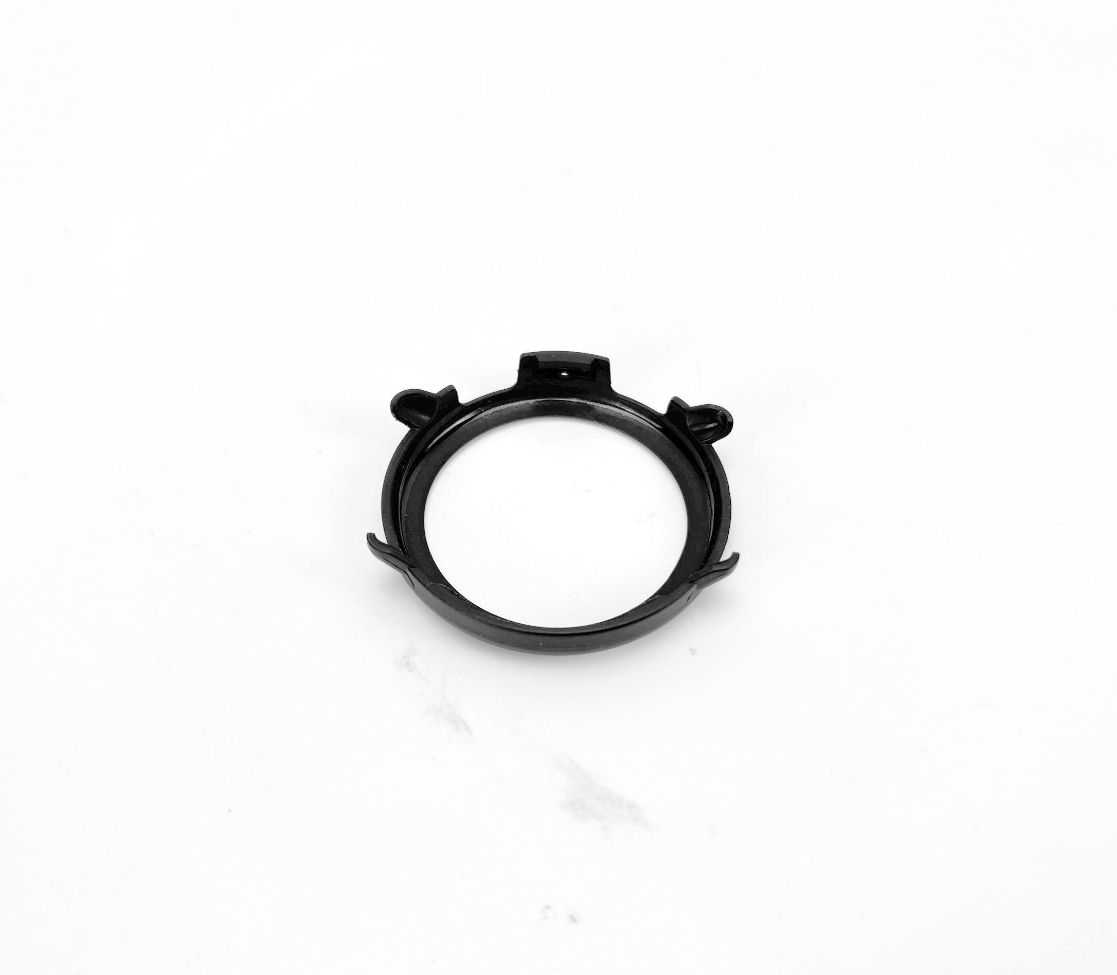 Cassa dell'orologio nera, circolare con ritagli e una piccola linguetta, su una superficie bianca.