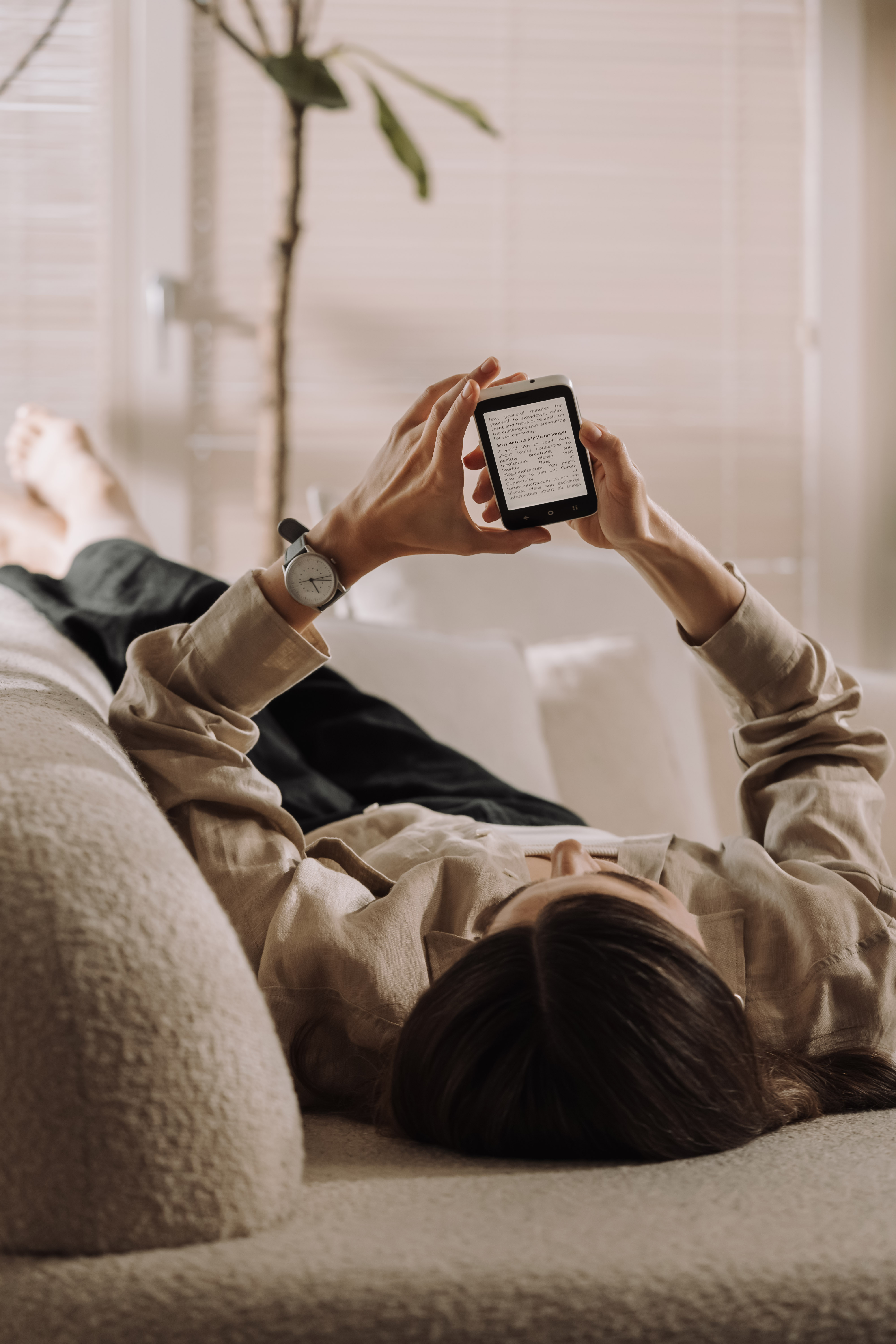 Eine Person liegt auf einer Couch und hält ein Smartphone, auf dem sie Text liest.