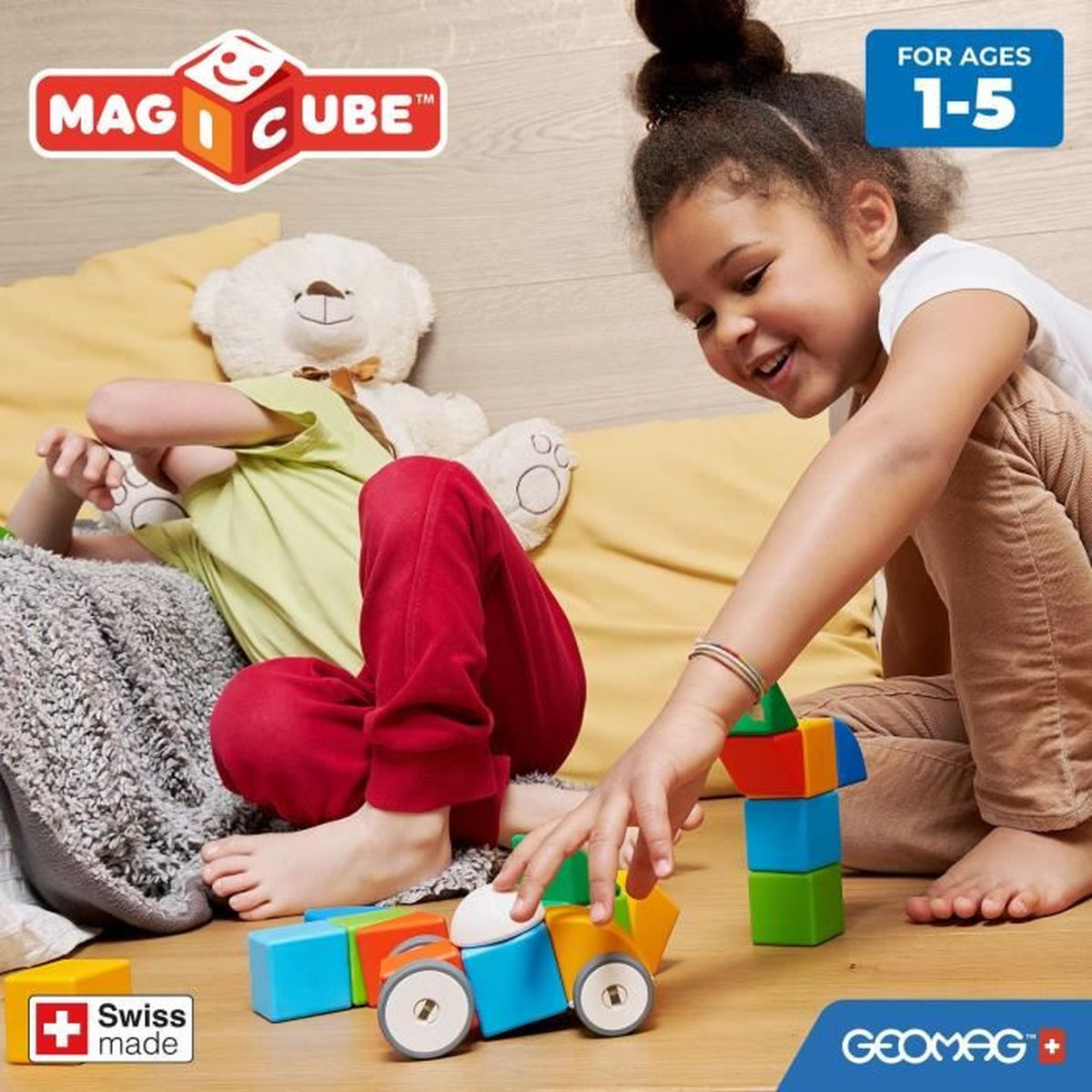 Ein Mädchen spielt mit Magcube-Spielzeugen und baut ein Auto, mit einem Teddybären und anderen Spielzeugen in der Nähe.