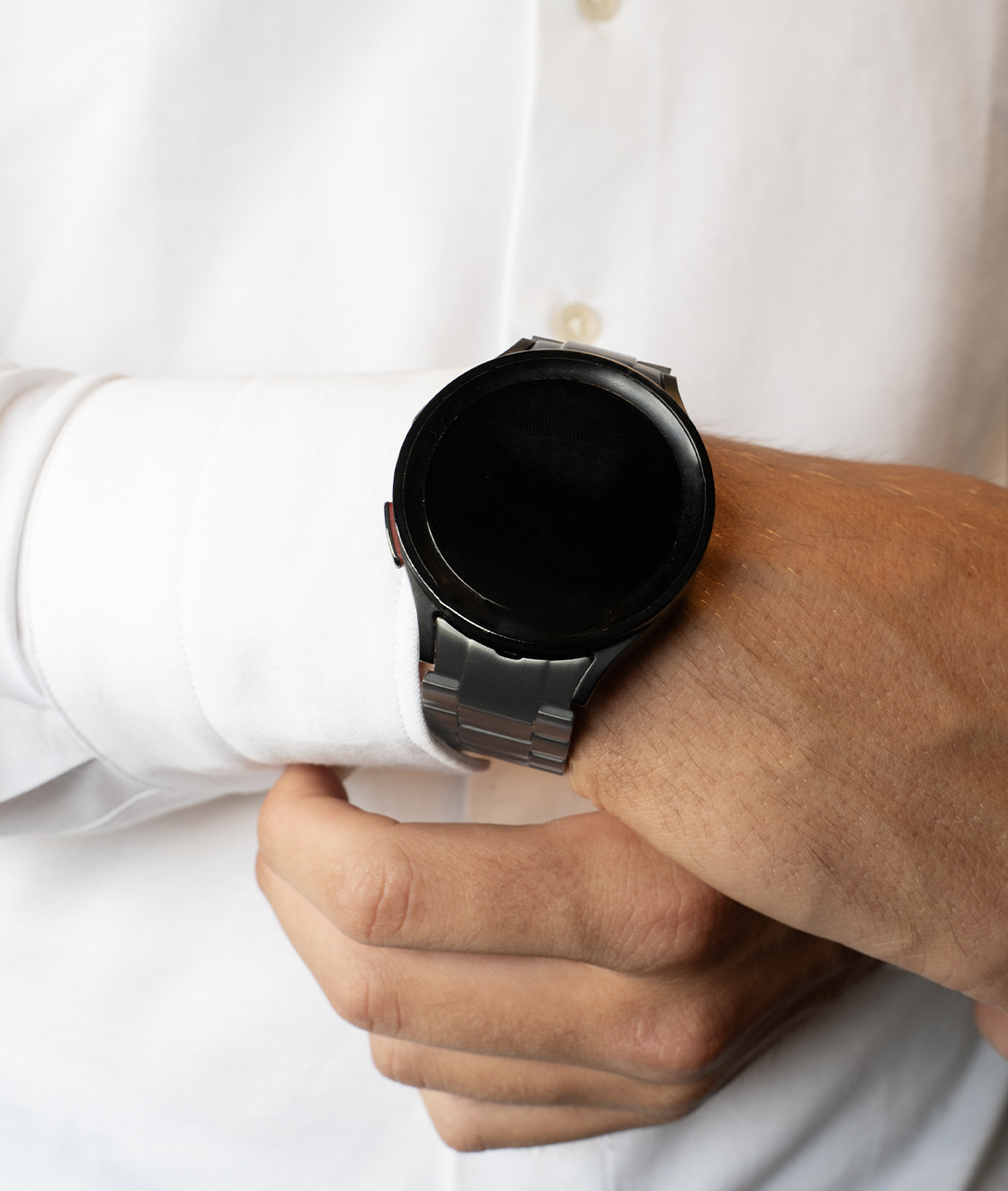 Das Handgelenk eines Mannes mit einer schwarzen Uhr. Die Uhr befindet sich am Handgelenk vor einem weißen Hemd. Der Hintergrund ist unscharf.