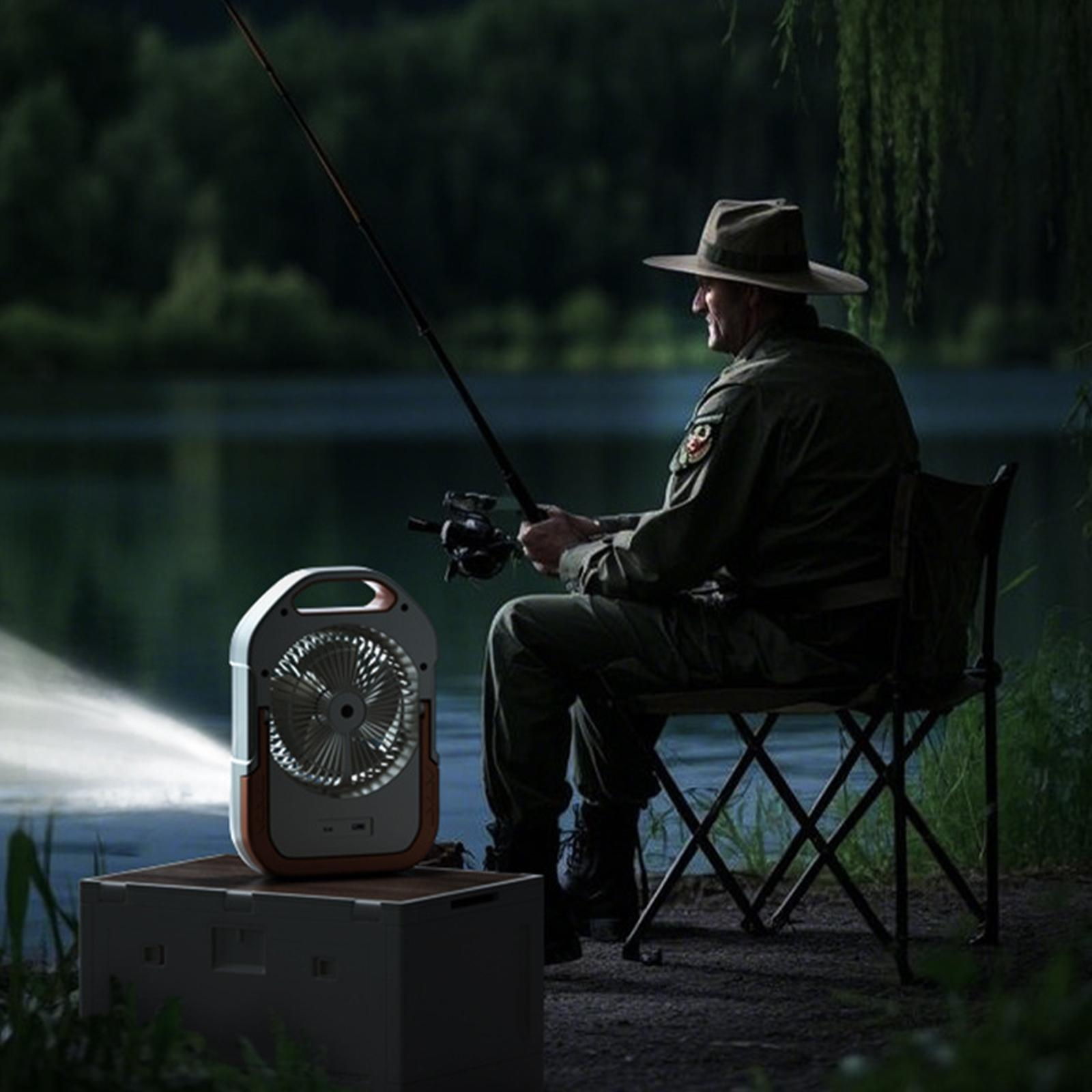 Ein Mann angelt nachts. Er sitzt auf einem Stuhl mit einem Ventilator, der Licht spendet. See im Hintergrund.