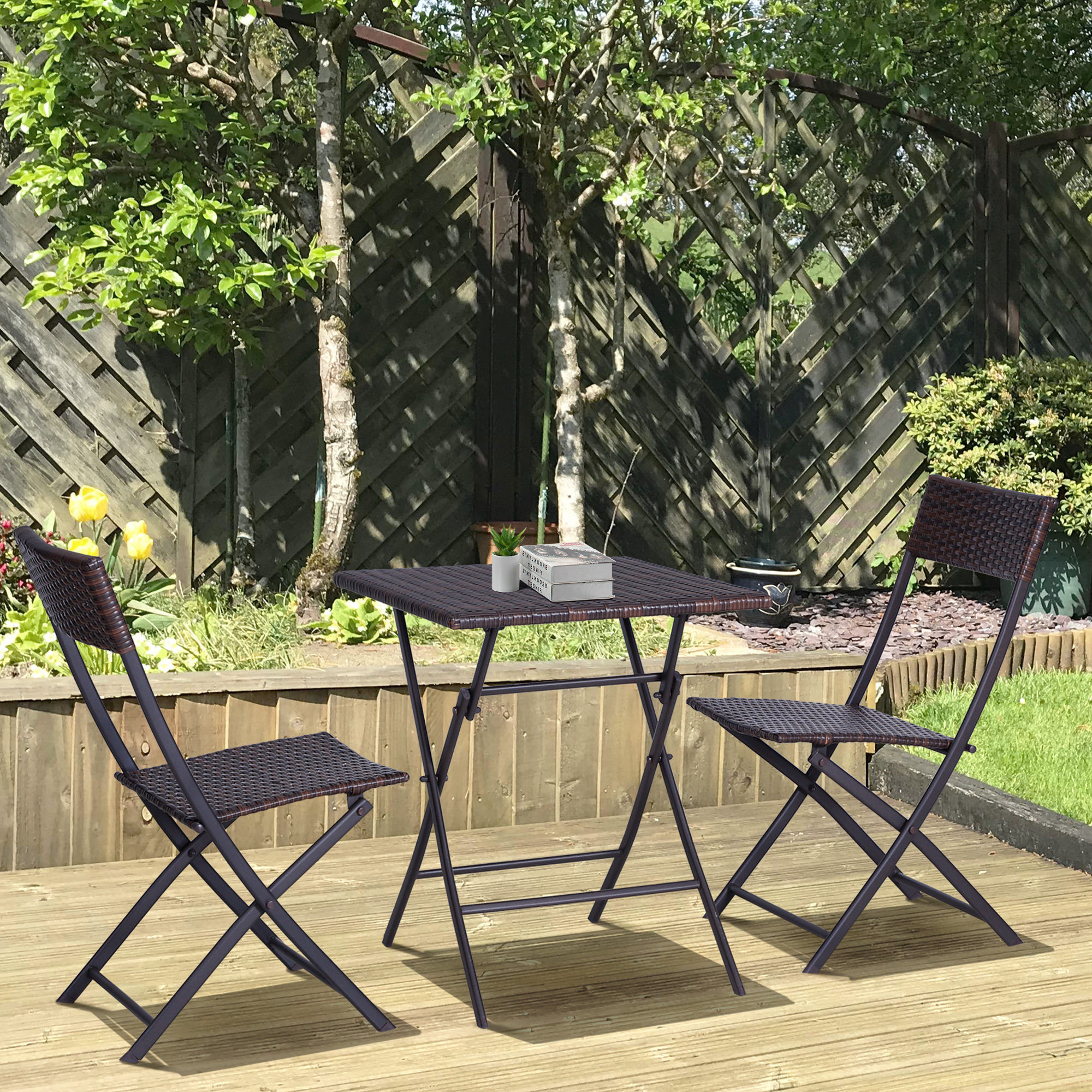 Terrassenmöbel-Set: zwei Stühle und ein Tisch auf einer Holzterrasse. Bäume und Zaun im Hintergrund.