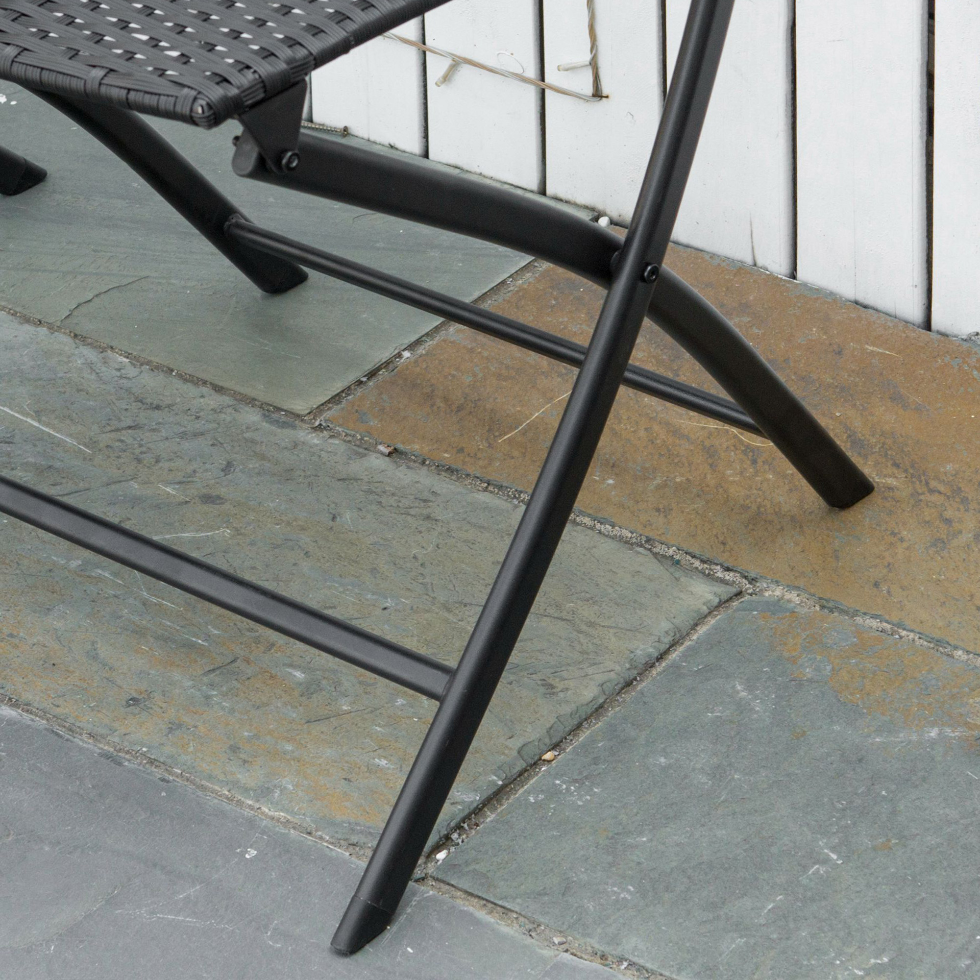 Nahaufnahme eines schwarzen Metall-Klappstuhlbeins auf einer Steinterrasse. Stuhl und Terrasse haben neutrale Farben.