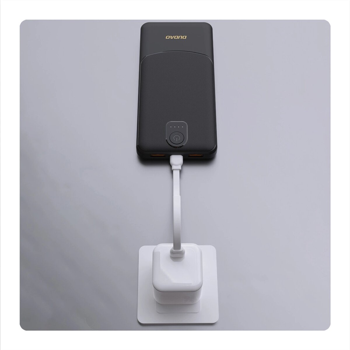 Czarny power bank z białą wtyczką do ładowania podłączoną do gniazdka. Power bank ma logo DUDO.