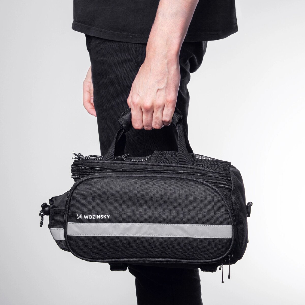 Eine Person hält eine schwarze Fahrradtasche mit Reflexstreifen. Die Tasche hat einen Griff und einen Reißverschluss.