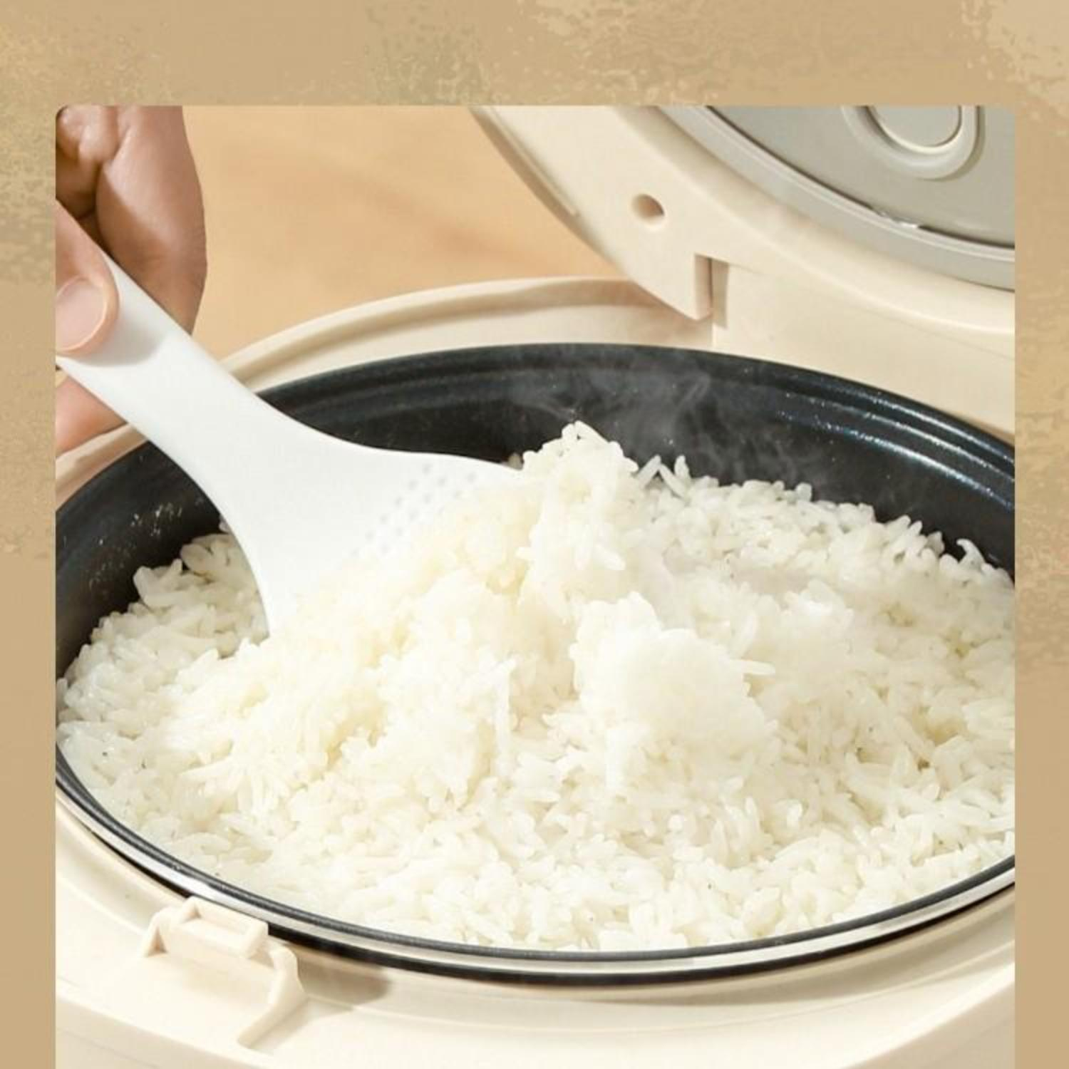 Eine Hand verwendet einen weißen Löffel, um Reis aus einem Reiskocher zu schöpfen. Der gekochte Reis ist sichtbar.