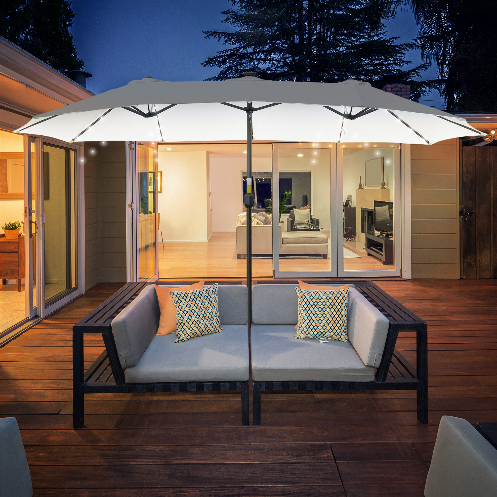 Eine Terrasse mit Doppelsitzcouch, Kissen und großem Sonnenschirm bei Nacht.
