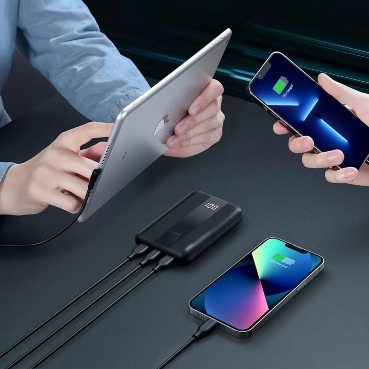 Hände halten Tablet und Smartphones. Powerbank mit 3 Kabeln im Vordergrund. Telefone laden.