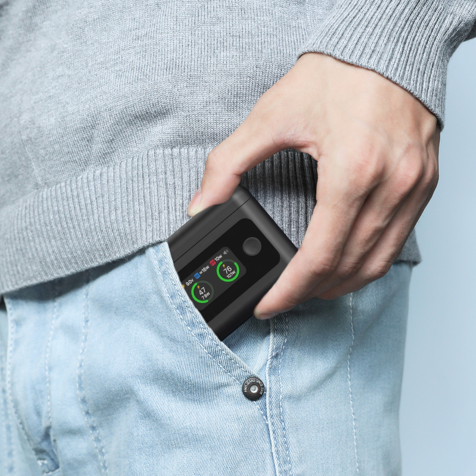 Person in einer Hosentasche, die eine schwarze Powerbank mit einem Bildschirm hält, der Ladestände zeigt, blaue Jeans.