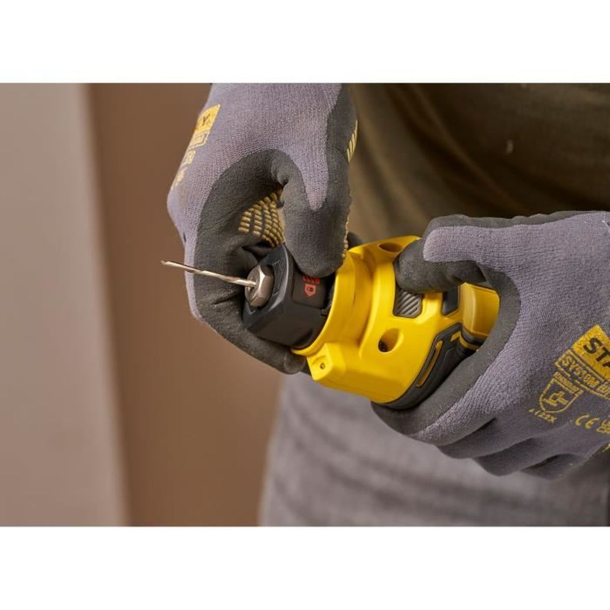 Hände mit Handschuhen halten ein gelbes Werkzeug. Eine Metallstange ragt aus der schwarzen Spitze.