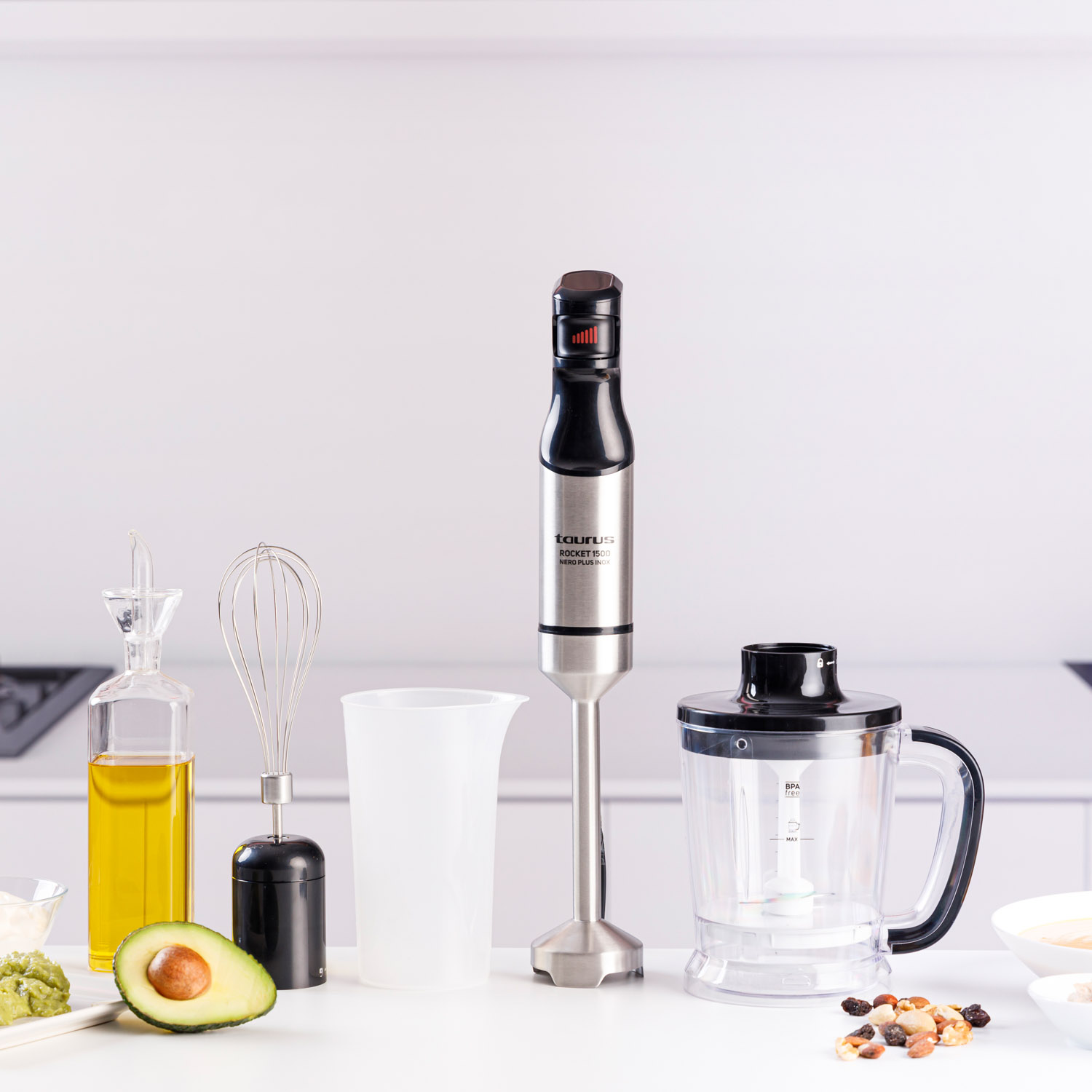 Eine Küchentheke mit Mixer, Schneebesen, Becher, Avocado, Öl und anderen Zutaten, alles bereit für die Zubereitung von Speisen.