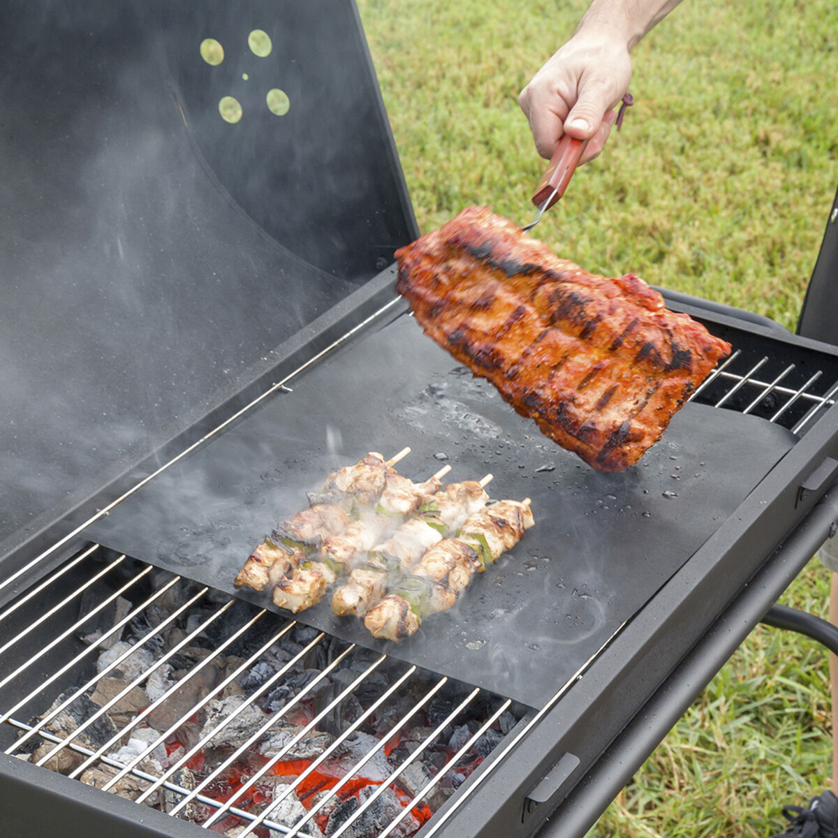 Una persona usa pinzas para levantar un trozo de carne cocida y a la parrilla de una parrilla.