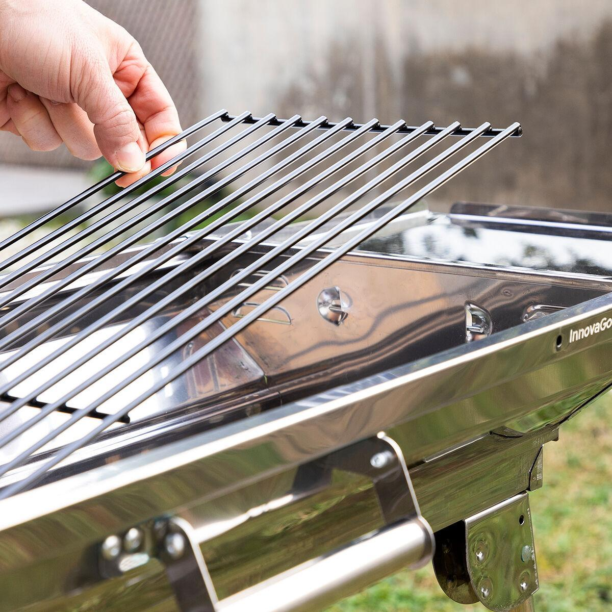 Eine Hand hält Grillstäbe über einem silbernen Grill. Der Grill befindet sich auf einem Gras Hintergrund.