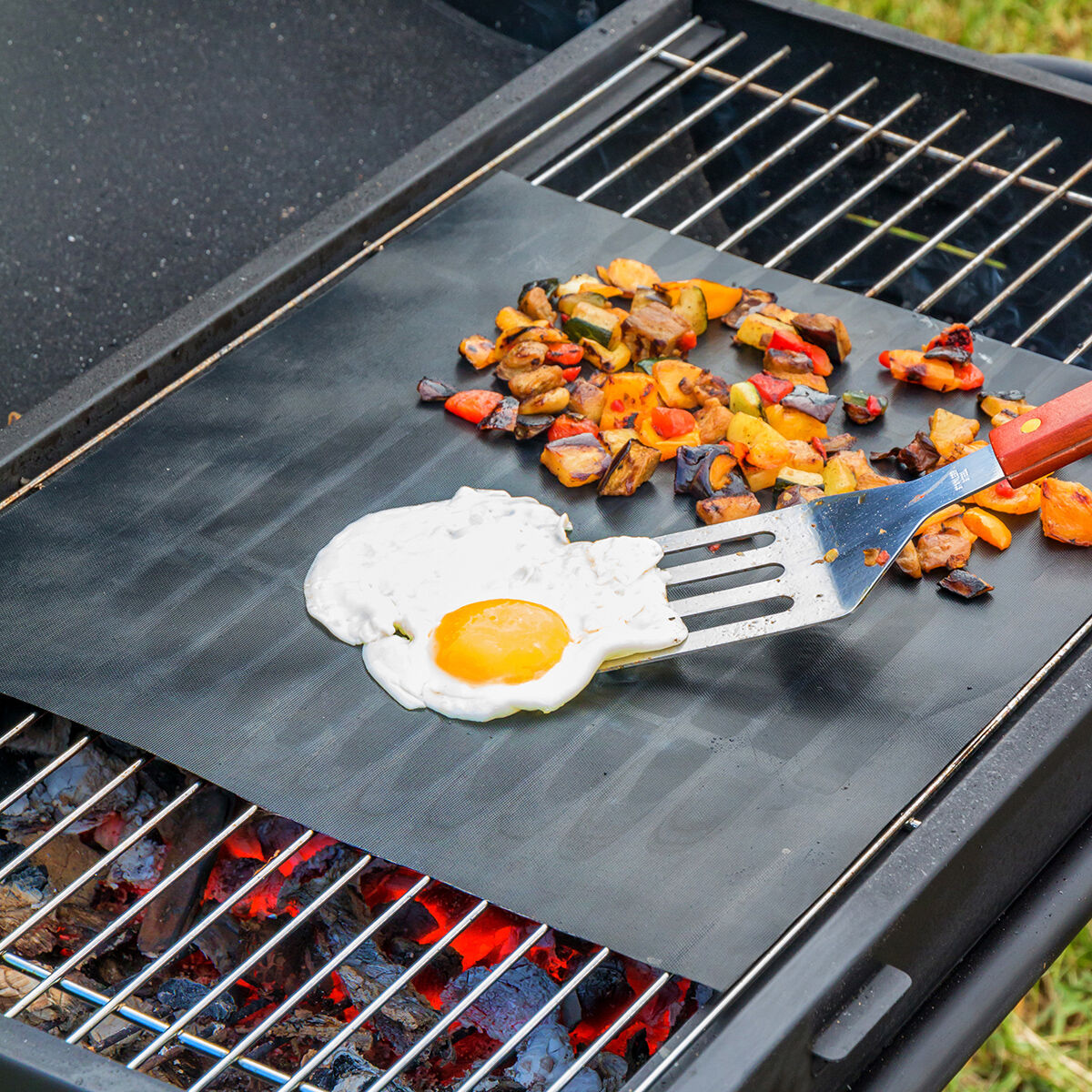 Un huevo frito y verduras a la parrilla sobre una alfombrilla negra en una parrilla.
