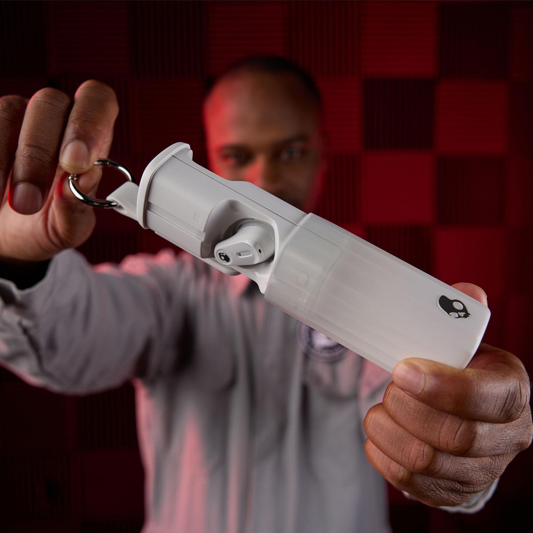 Mężczyzna trzymający białe słuchawki i etui ładujące, zwrócony w stronę kamery.