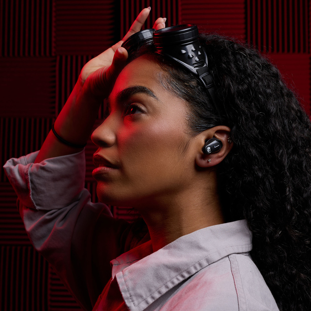 Kobieta ze słuchawkami, wkładką douszną w uchu, czerwonym tłem ściany.