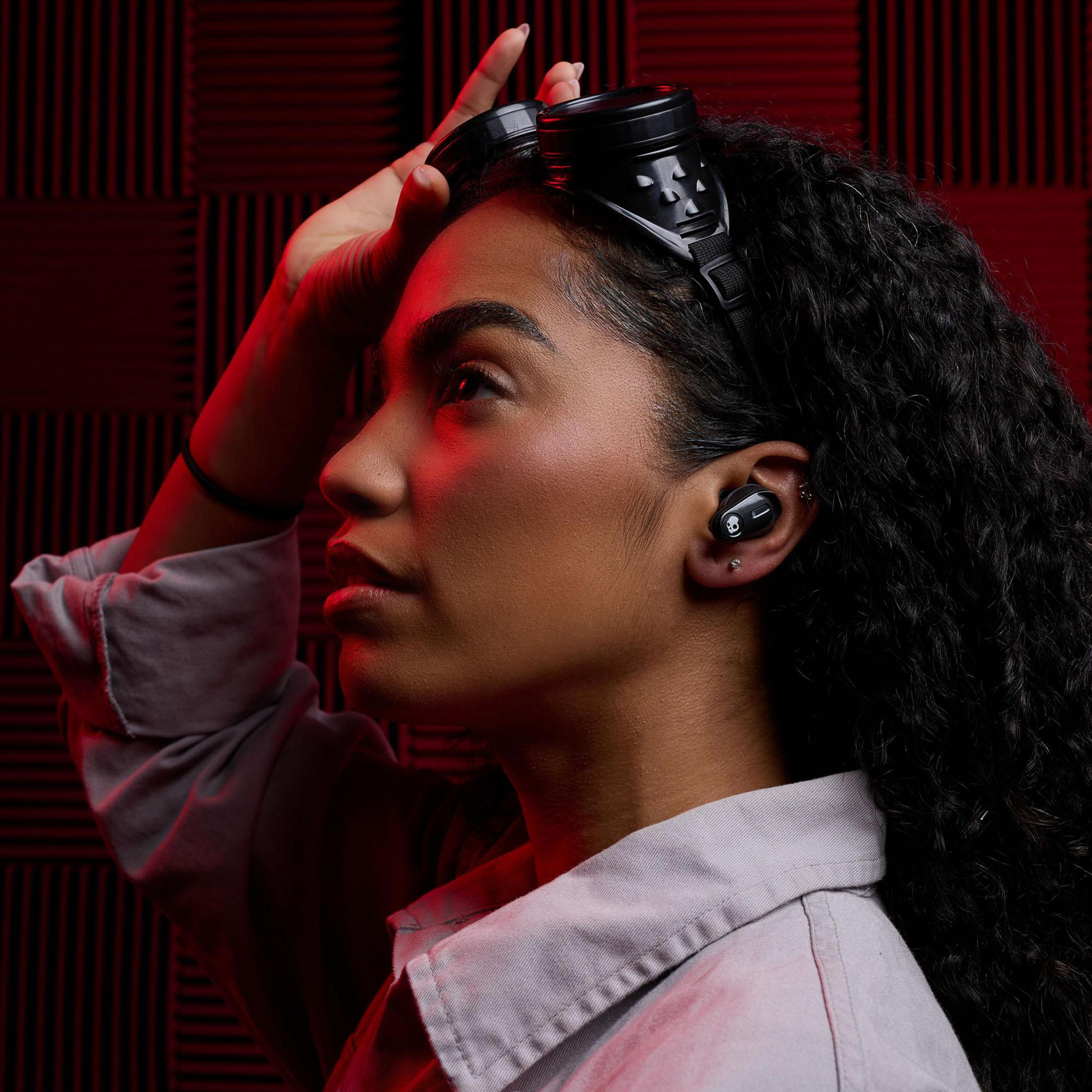 Kobieta ze słuchawkami, wkładką douszną w uchu, czerwonym tłem ściany.