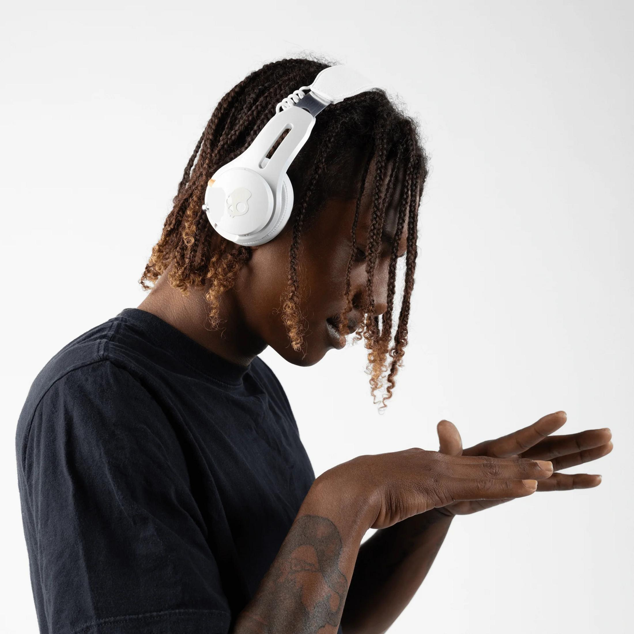 Osoba z warkoczami nosi białe słuchawki i patrzy na dłonie.