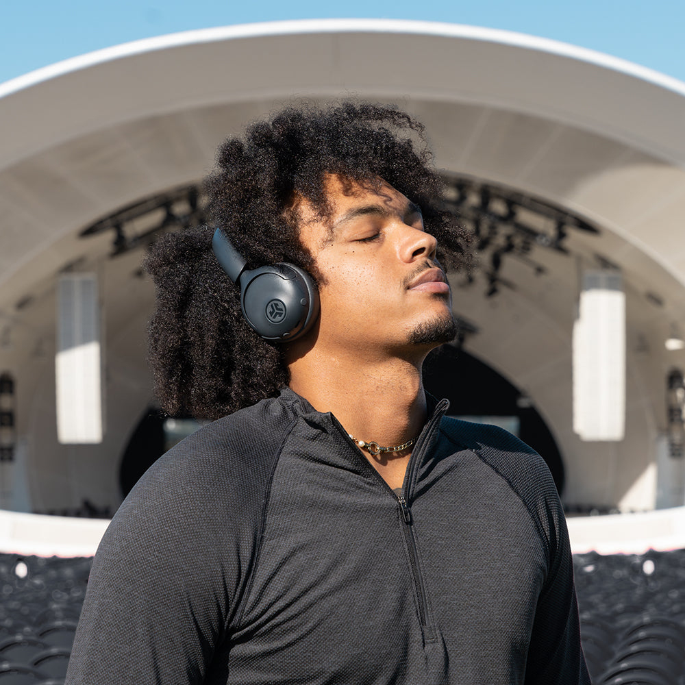Homme aux cheveux bouclés portant un casque noir, yeux fermés, devant une scène.