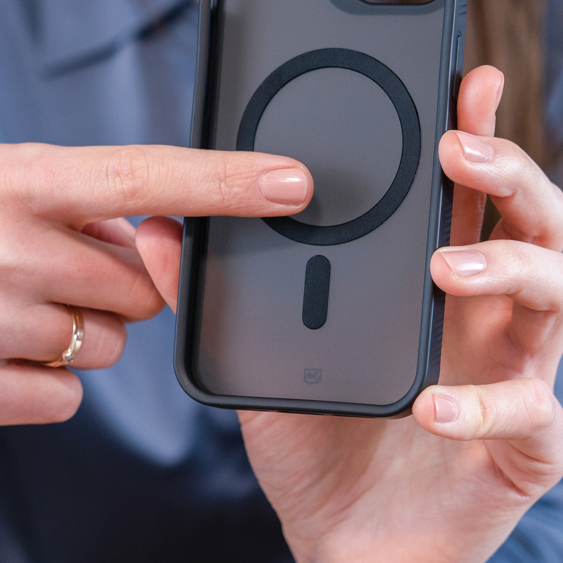 Osoba trzyma etui na telefon z czarnym pierścieniem. Palce trzymają etui, a pierścień jest z tyłu.