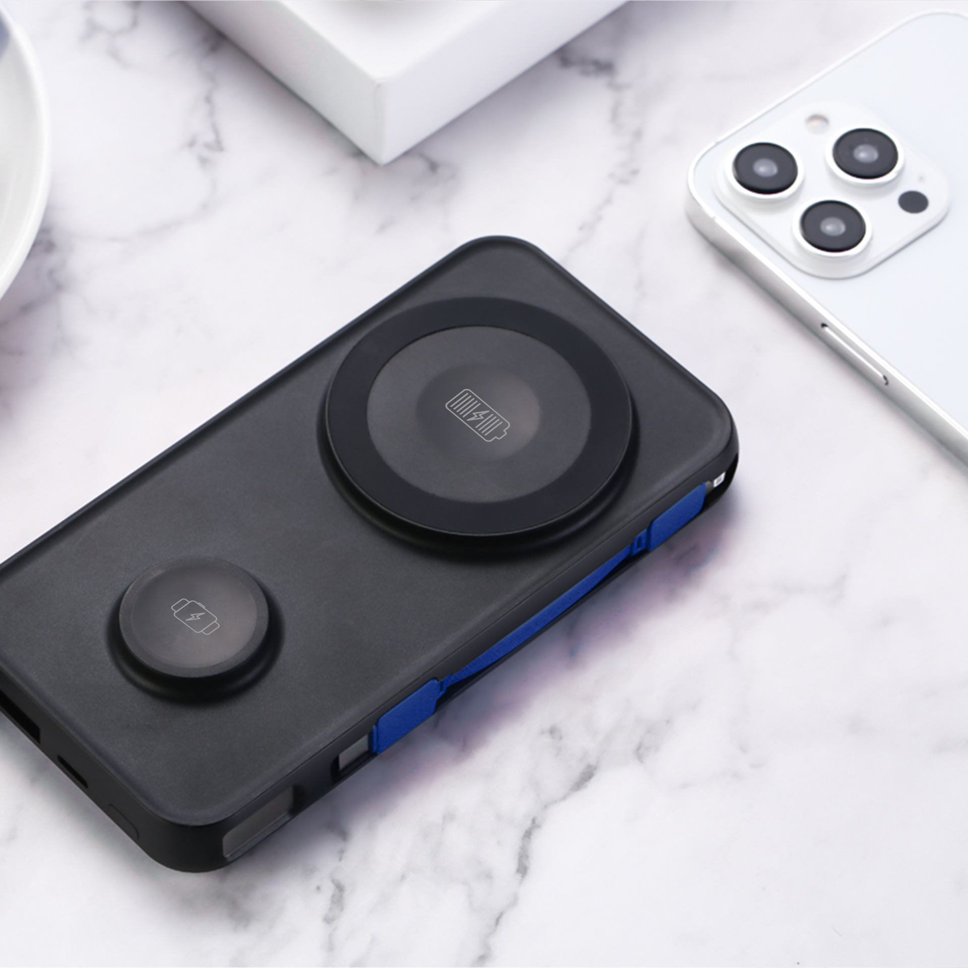 Czarny power bank z podkładką ładującą. Telefon jest na podkładce. Czarno-białe marmurowe tło.