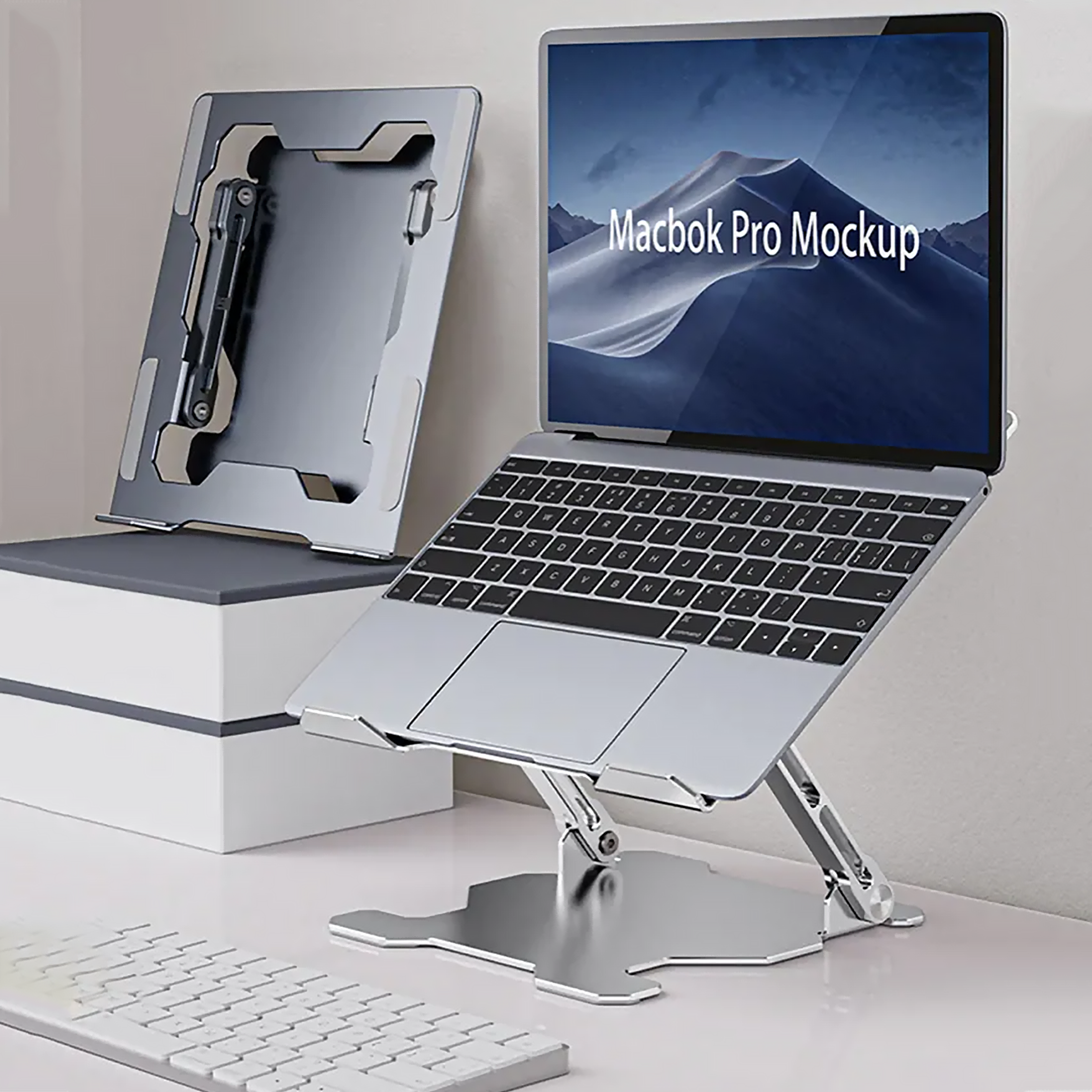 Laptop auf silbernem Ständer, Tastatur und ein weiterer Ständer im Hintergrund. Weißer Schreibtisch, weiße Box und Bildschirm.