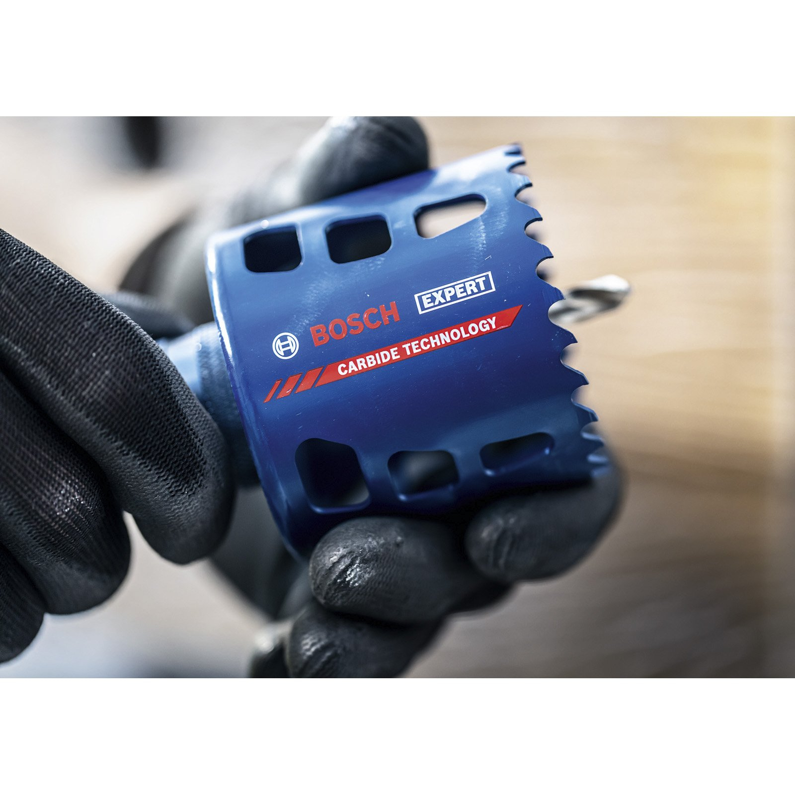 Zbliżenie niebieskiej piły otwornicy Bosch Expert trzymanej w rękawicach. Technologia Carbide.