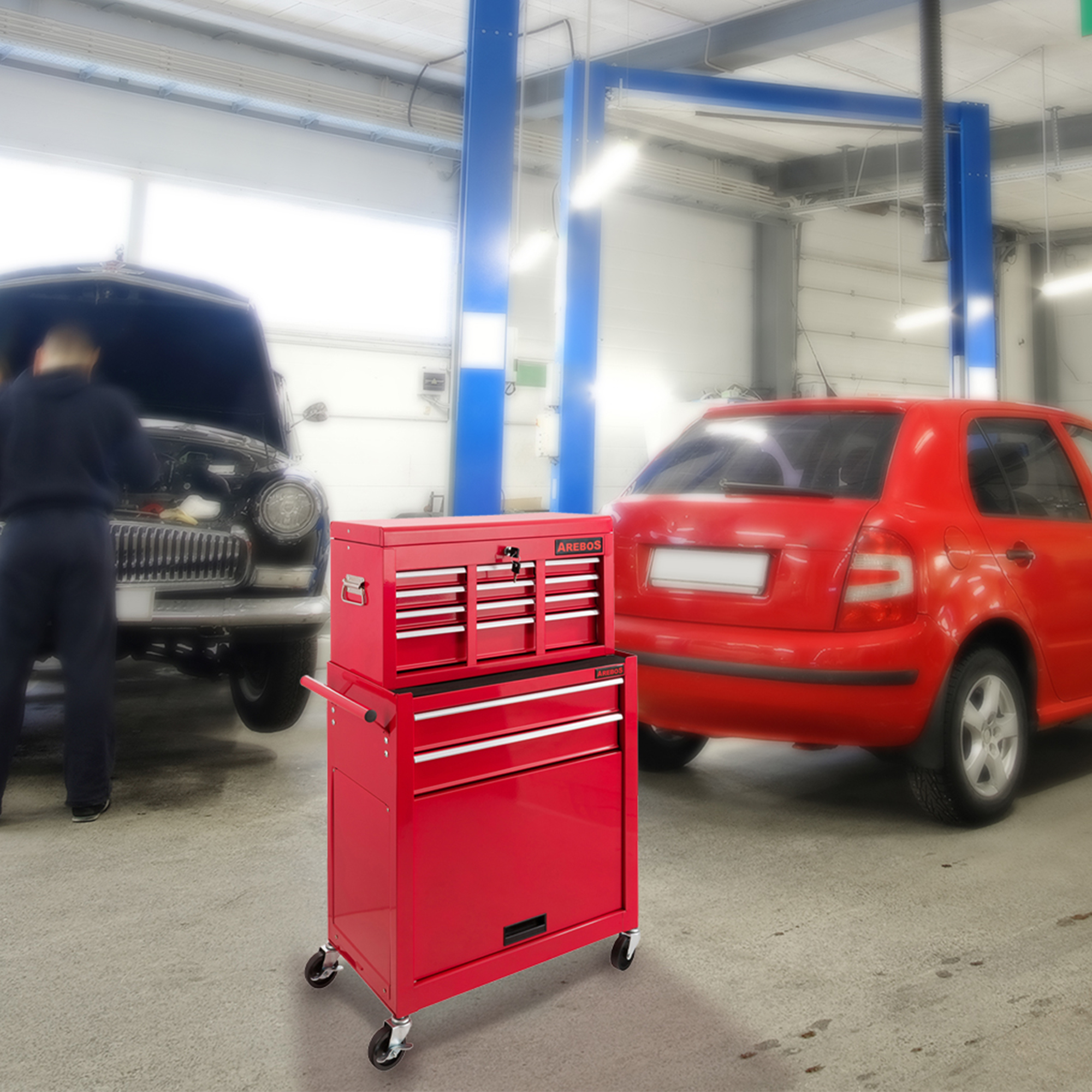 Ein roter Werkzeugkasten in einer Garage. Ein Mechaniker arbeitet im Hintergrund an einem Auto. Ein rotes Auto ist ebenfalls sichtbar.