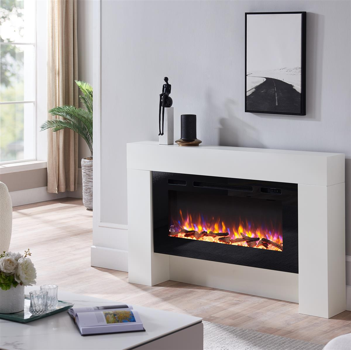 Ein weißer elektrischer Kamin in einem Wohnzimmer. Es gibt ein Fenster, eine Couch, ein Gemälde und einen Couchtisch.