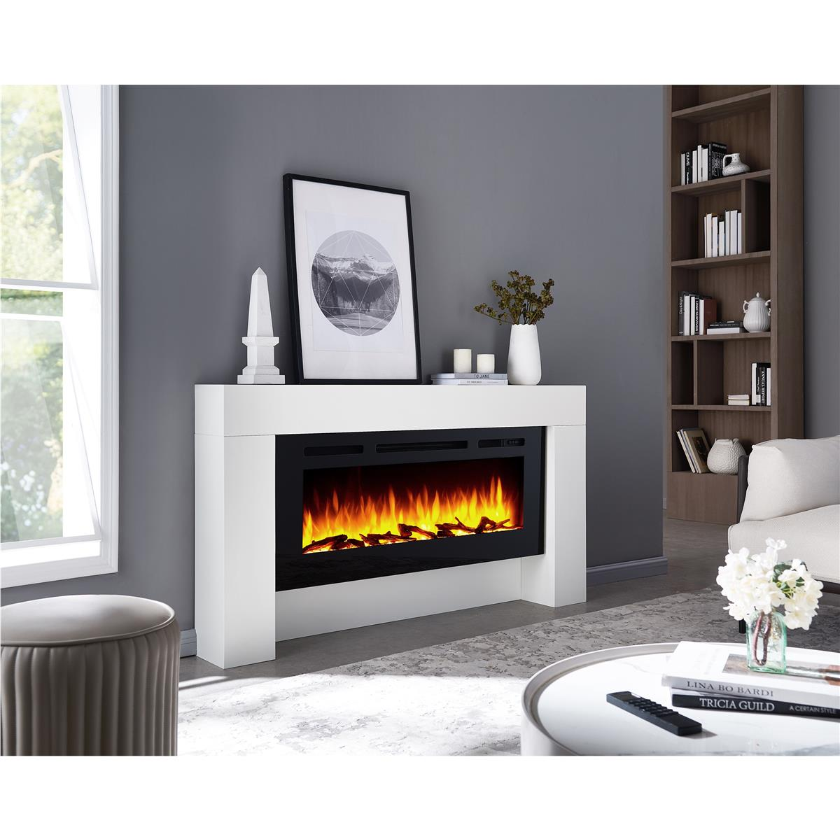 Ein weißer elektrischer Kamin in einem Wohnzimmer mit orangefarbenen Flammen. Es gibt ein Sofa, einen Tisch und Bücher.